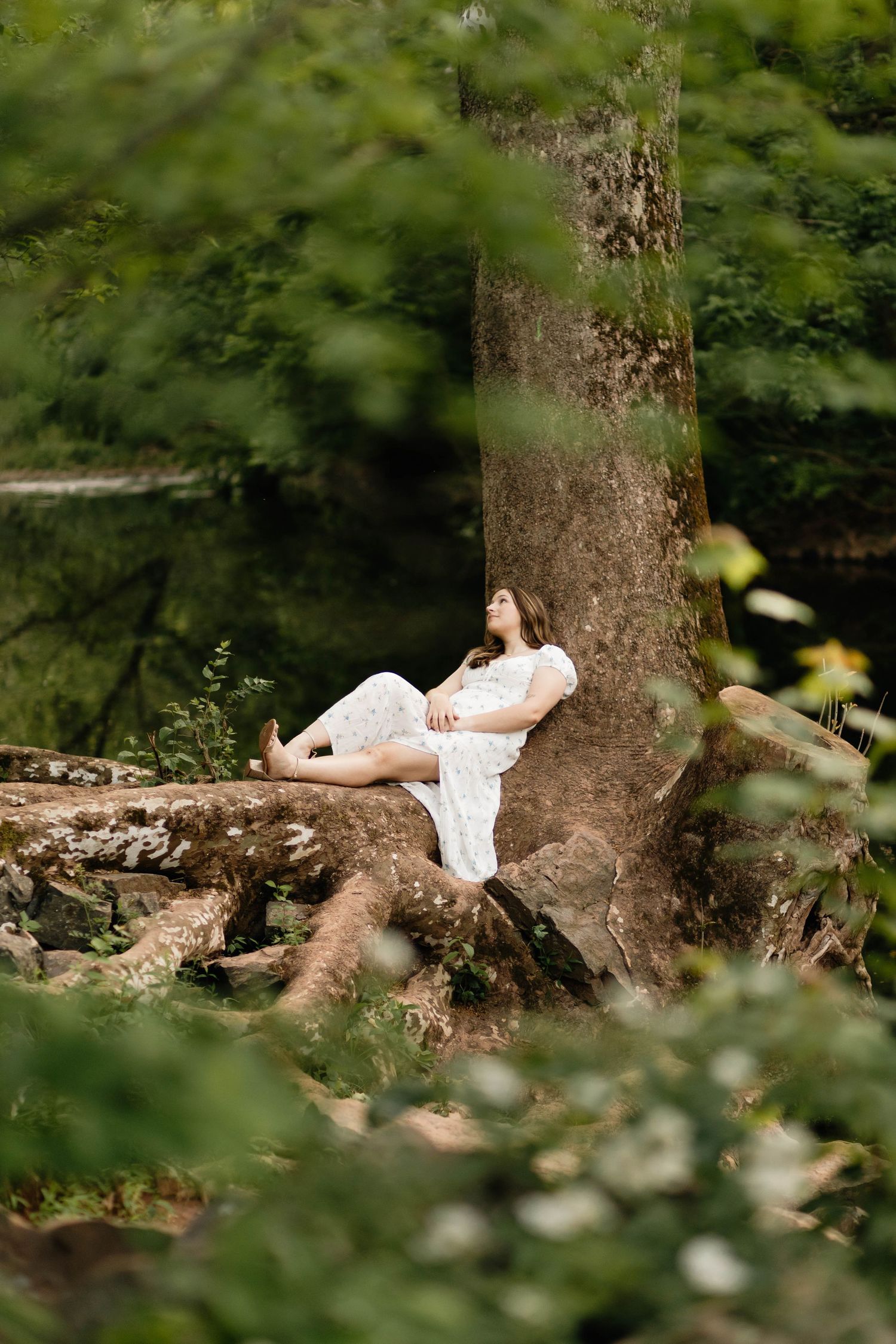 Boyertown Senior in white dress reclines peacefully against large tree in forest in Harleysville, PA.