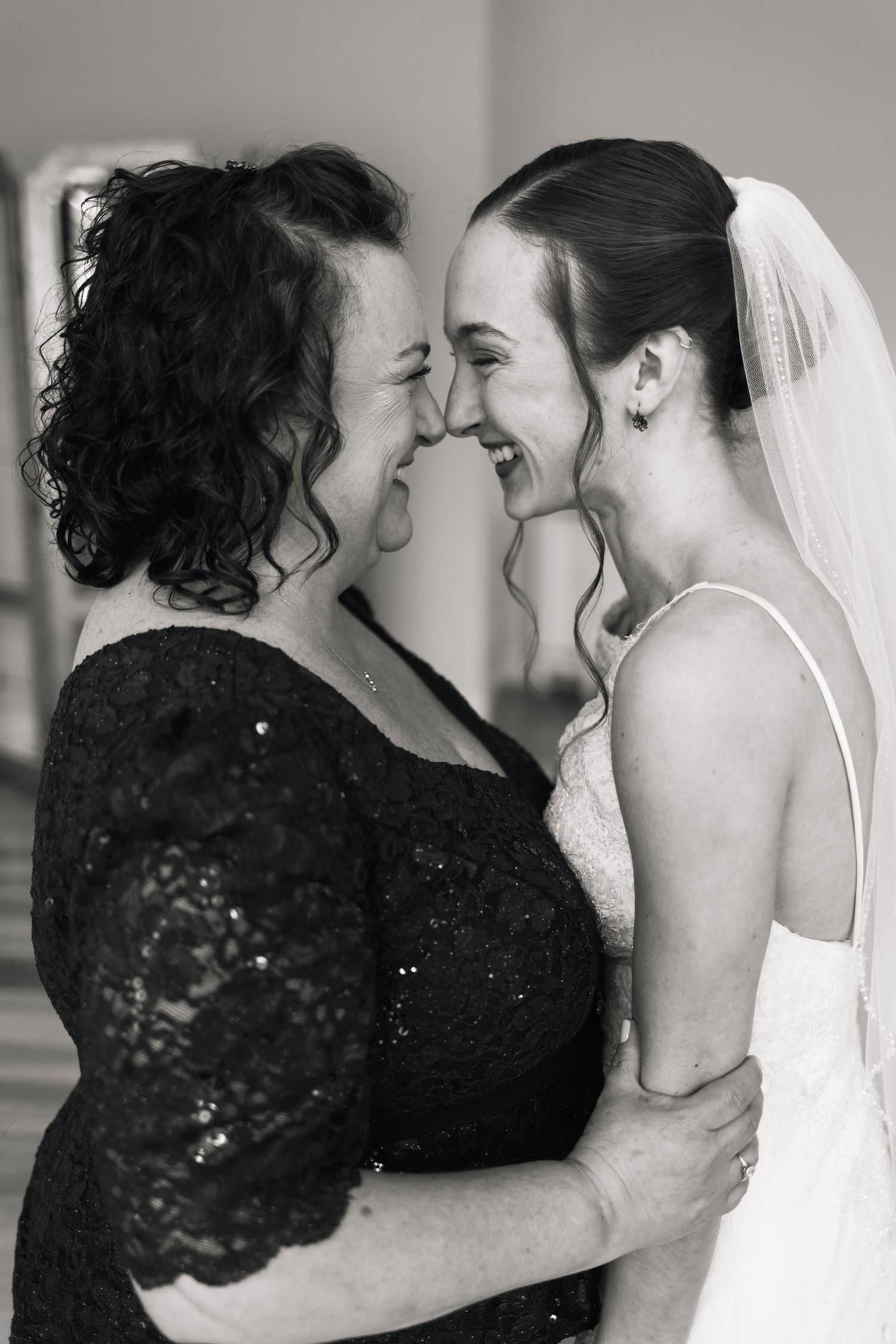 Black and white photo of bride and mother sharing a joyful laugh while embracing before wedding.