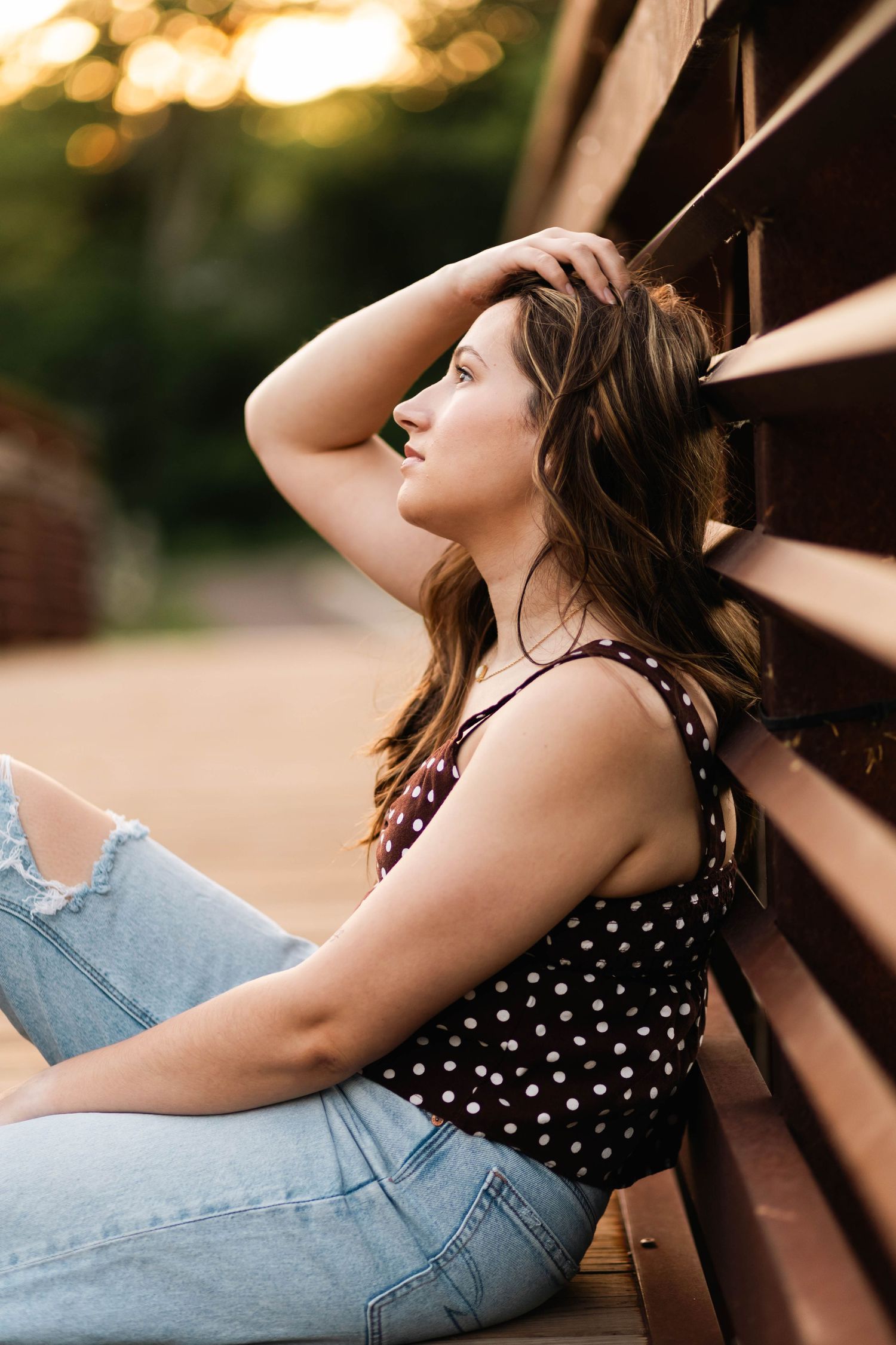 Boyertown High School Senior in polka dot top and jeans leaning against bridge ingolden hour light at Fischer Park in Harleysville, PA.