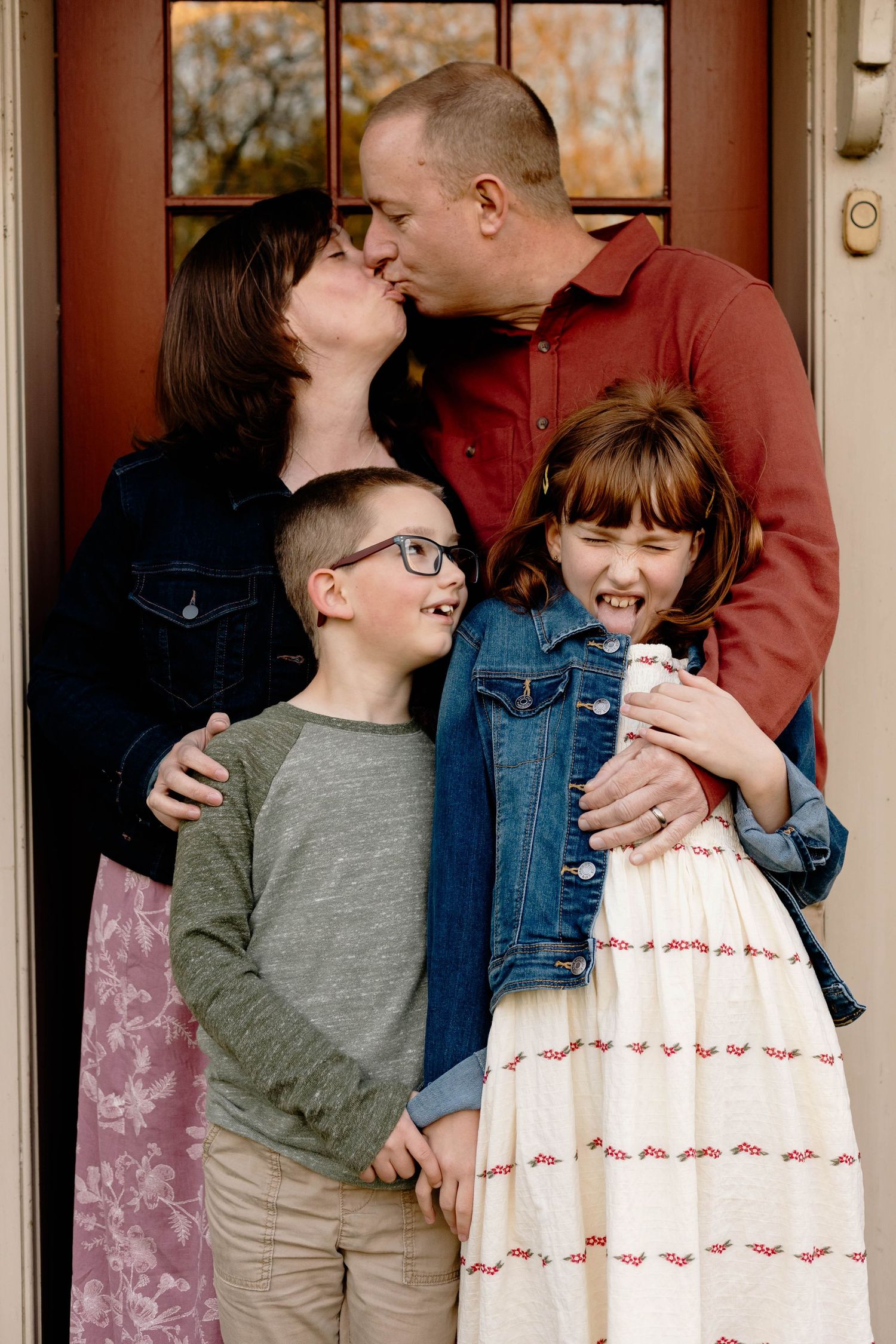 A family of four shares a warm moment at their front door, parents kissing while children smile and laugh in Elverson, PA.