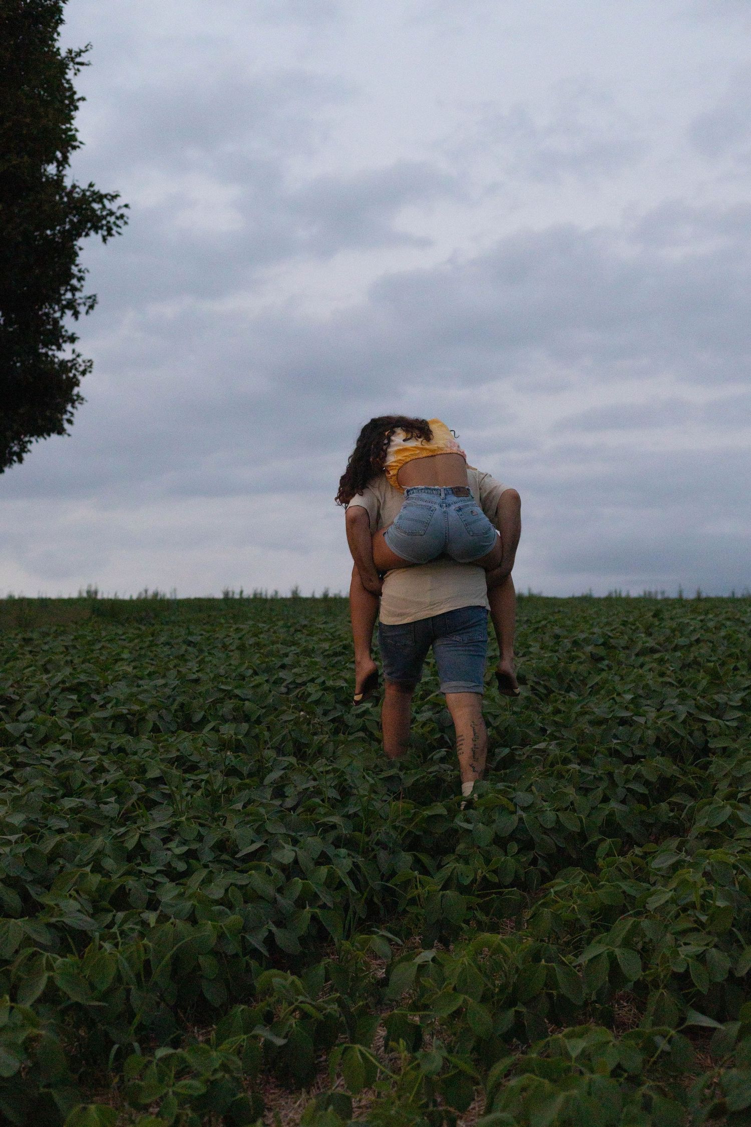 A man carries a woman piggyback through a lush green field under a cloudy sky in Elverson, PA.