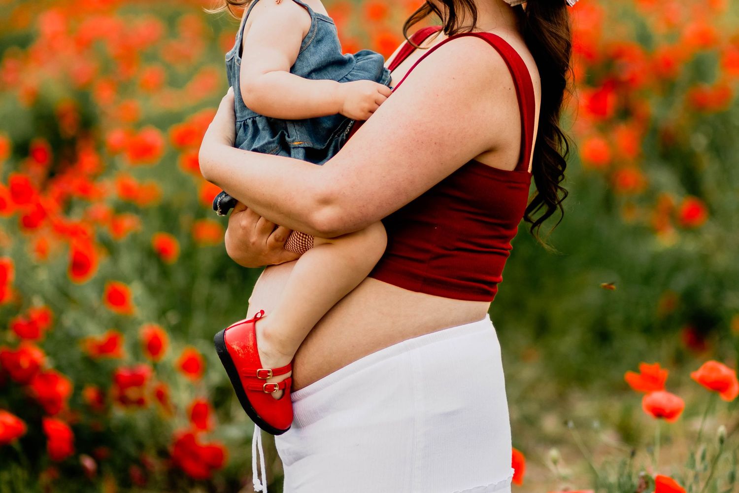 Maternity session with expecting mother holding a young child at a red poppy flower field at Levengood Flowers in Douglassville, PA.