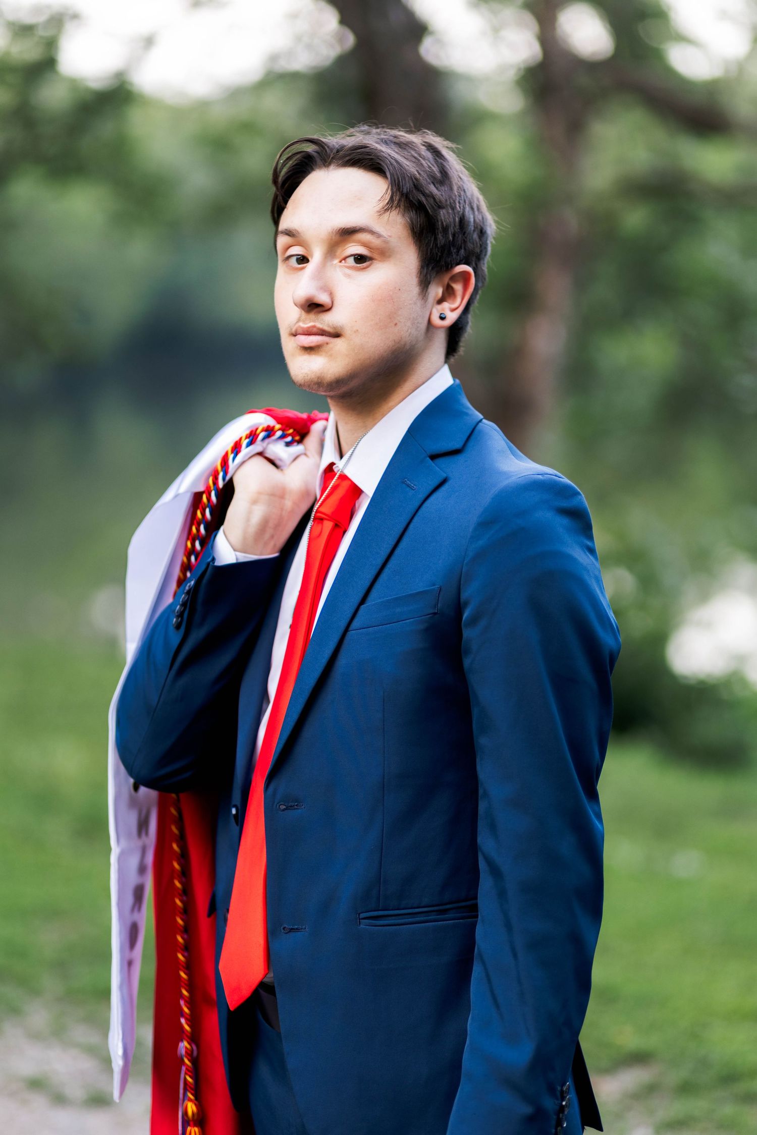 Owen J Roberts High School Senior in navy suit with red tie holds graduation stole over shoulder outdoors.
