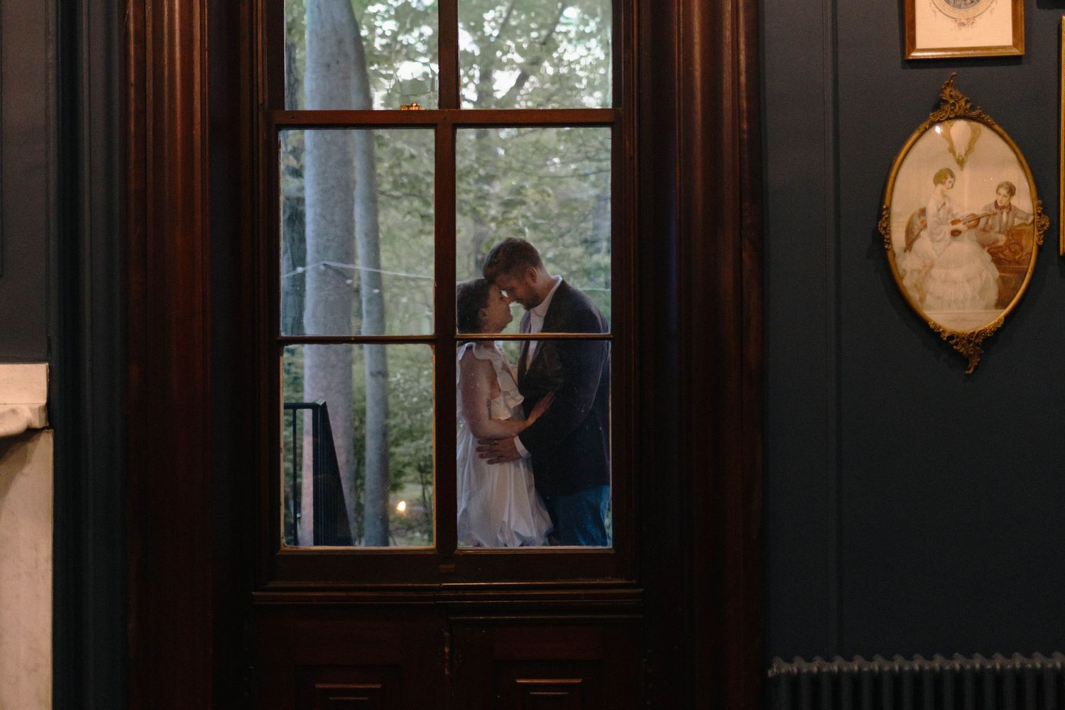 Couple sharing a romantic kiss framed by elegant wooden doors with trees in background in West Chester, PA.