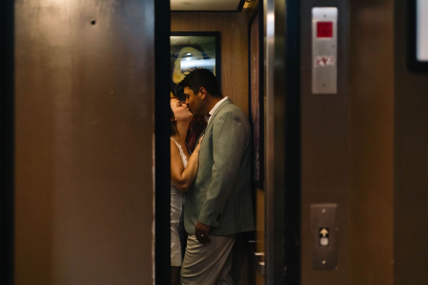 Bride and groom sharing an intimate moment kissing inside an elevator with doors open.