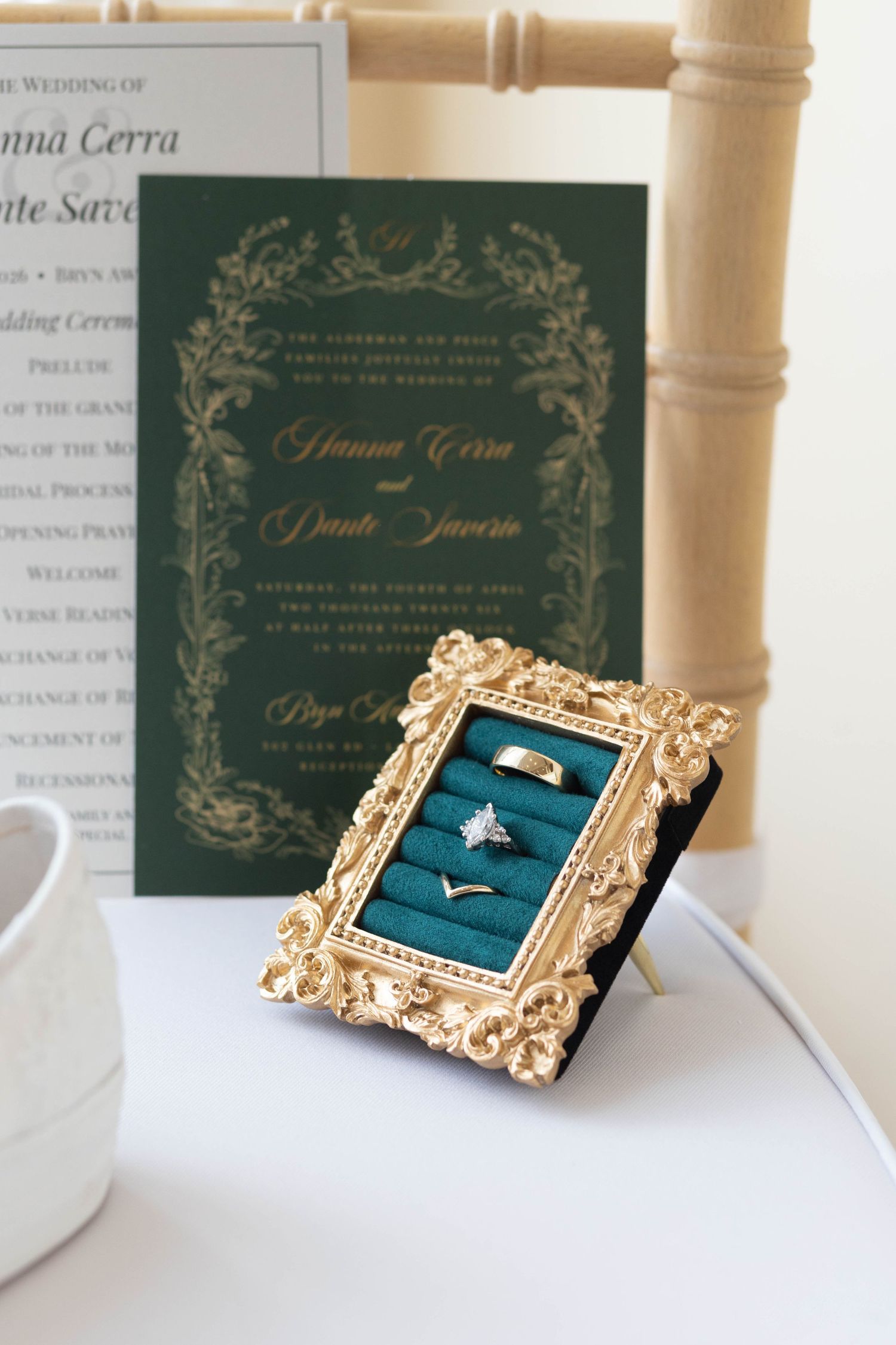 Elegant emerald green and gold wedding invitation displayed beside ornate ring box with wedding rings.