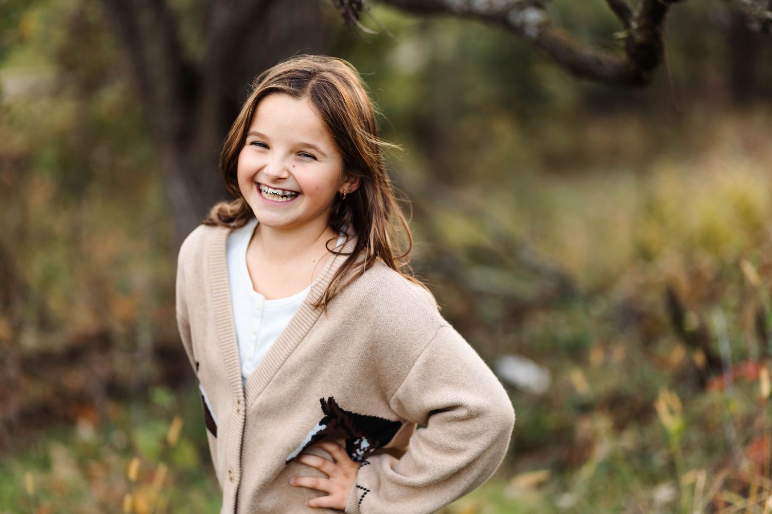 A young girl with braces smiles confidently outdoors wearing a beige cardigan in autumn in Harleysville, PA.