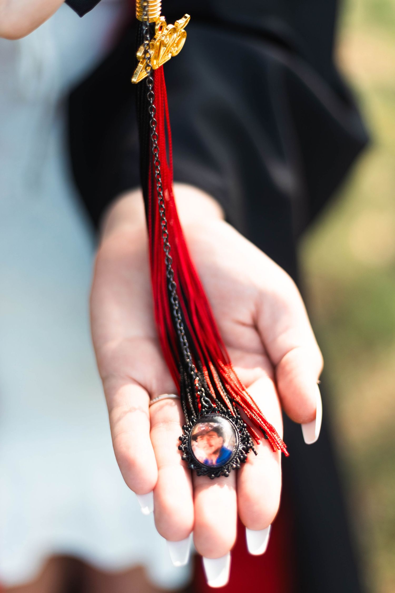 Close-up of a hand holding a graduation tassel with red and black strands and a small photo charm pendant.