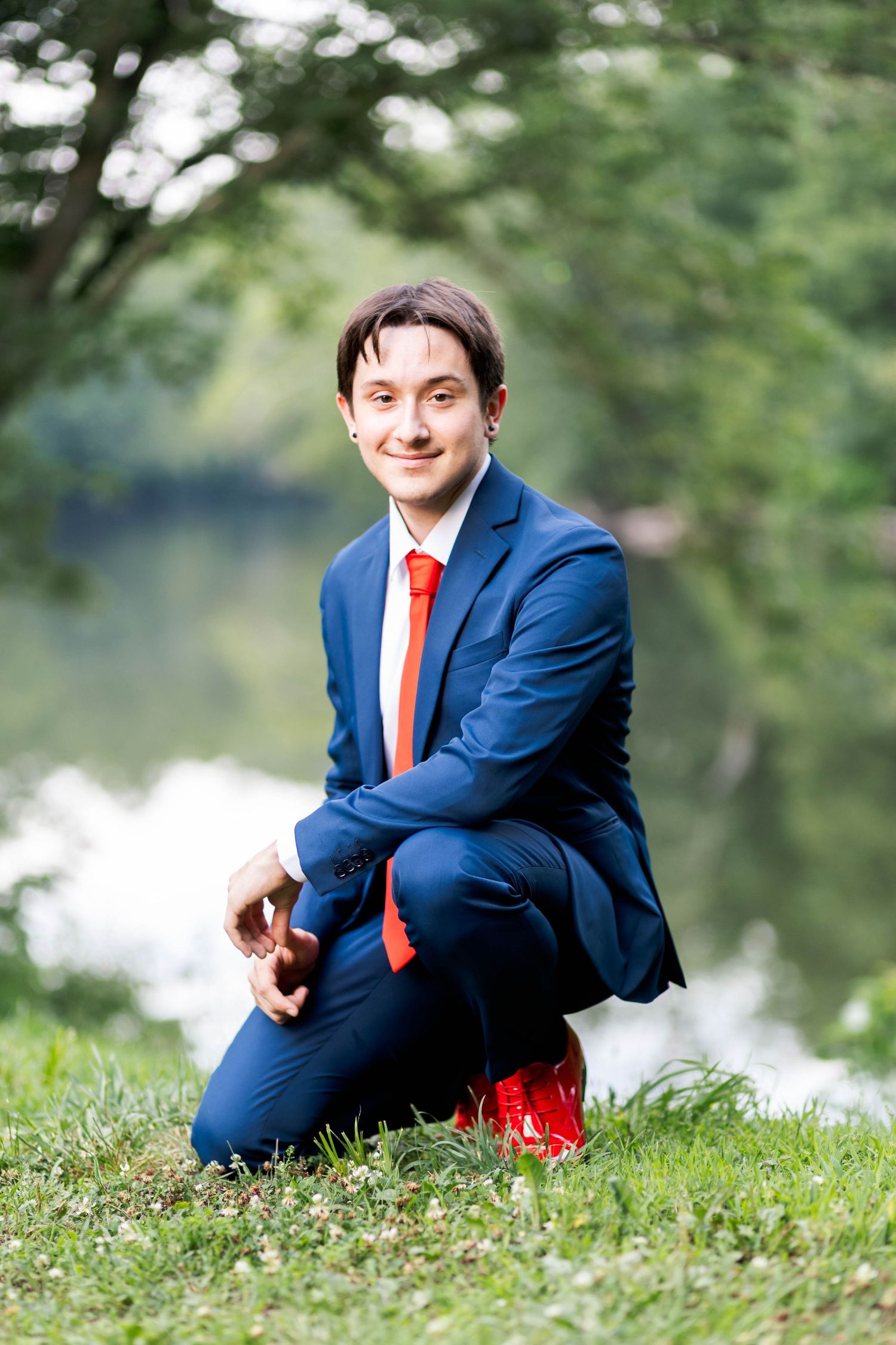 Owen J Roberts High School Senior in blue suit with red tie crouching on grass near pond in Pottstown, PA