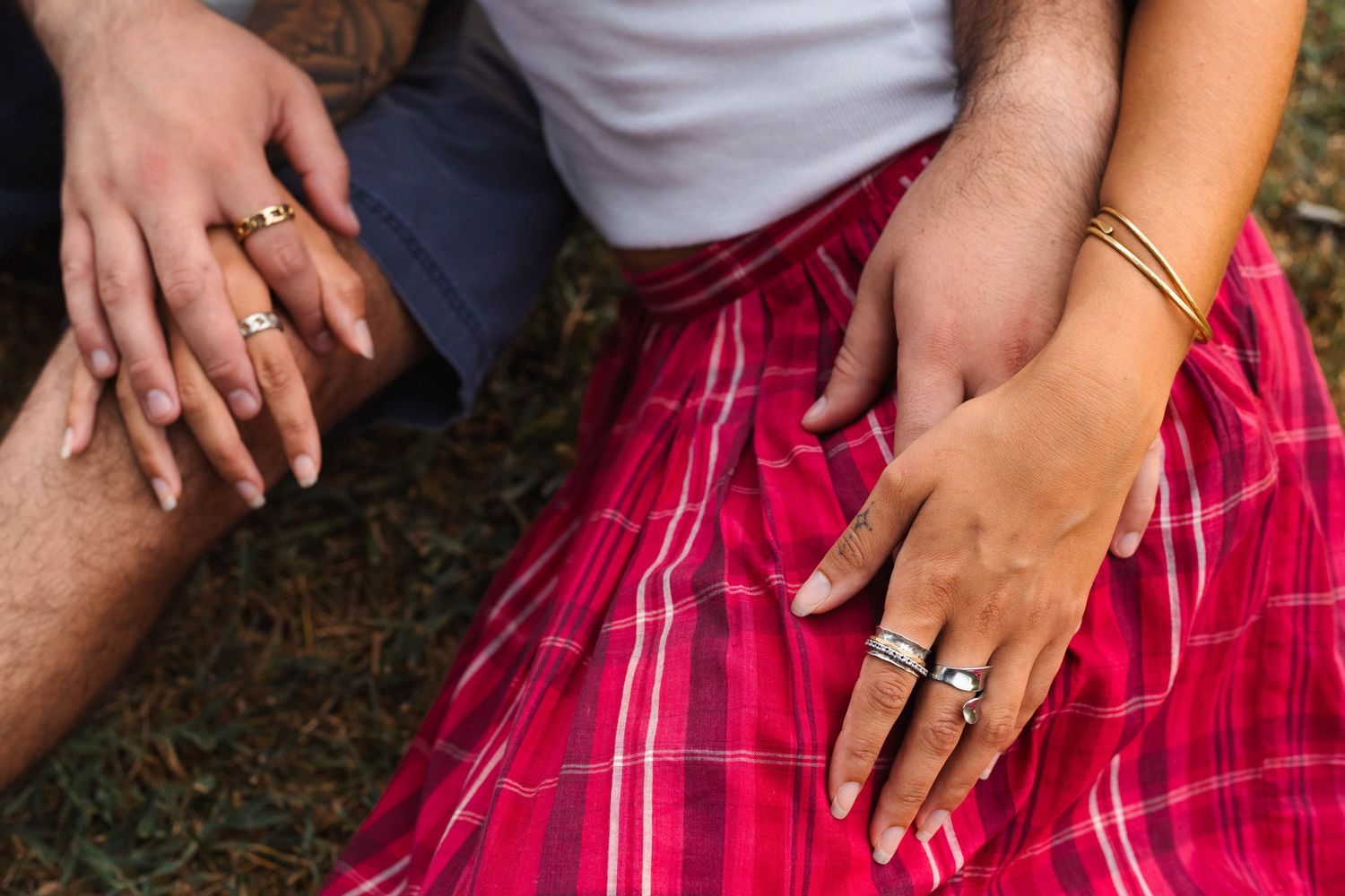Close-up of an engaged couple's hands with rings resting on a red plaid skirt outdoors during an engagement session in Elverson, PA.