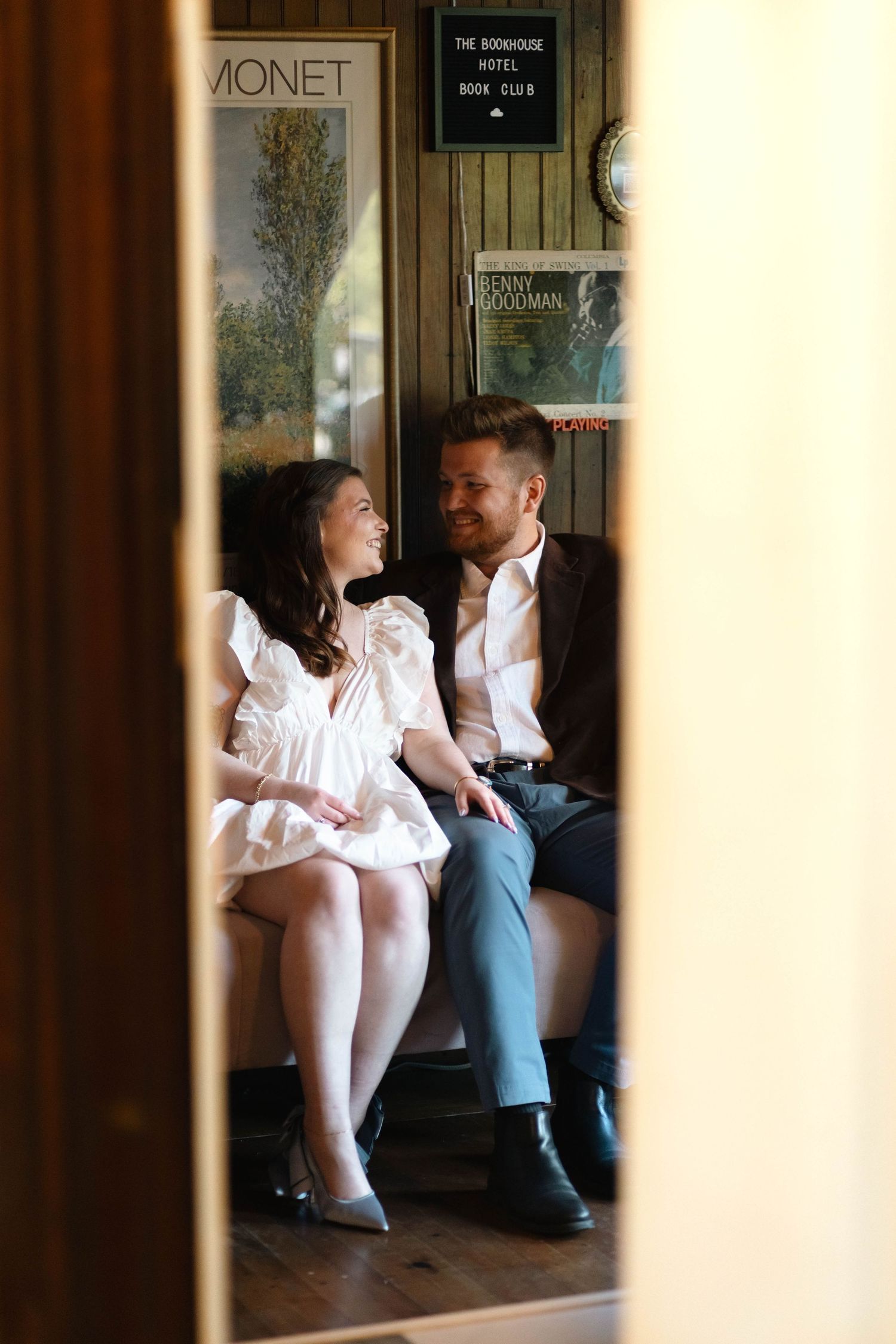 Couple sitting together on a bench, smiling at each other inside a cozy vintage hotel lounge in West Chester, PA.
