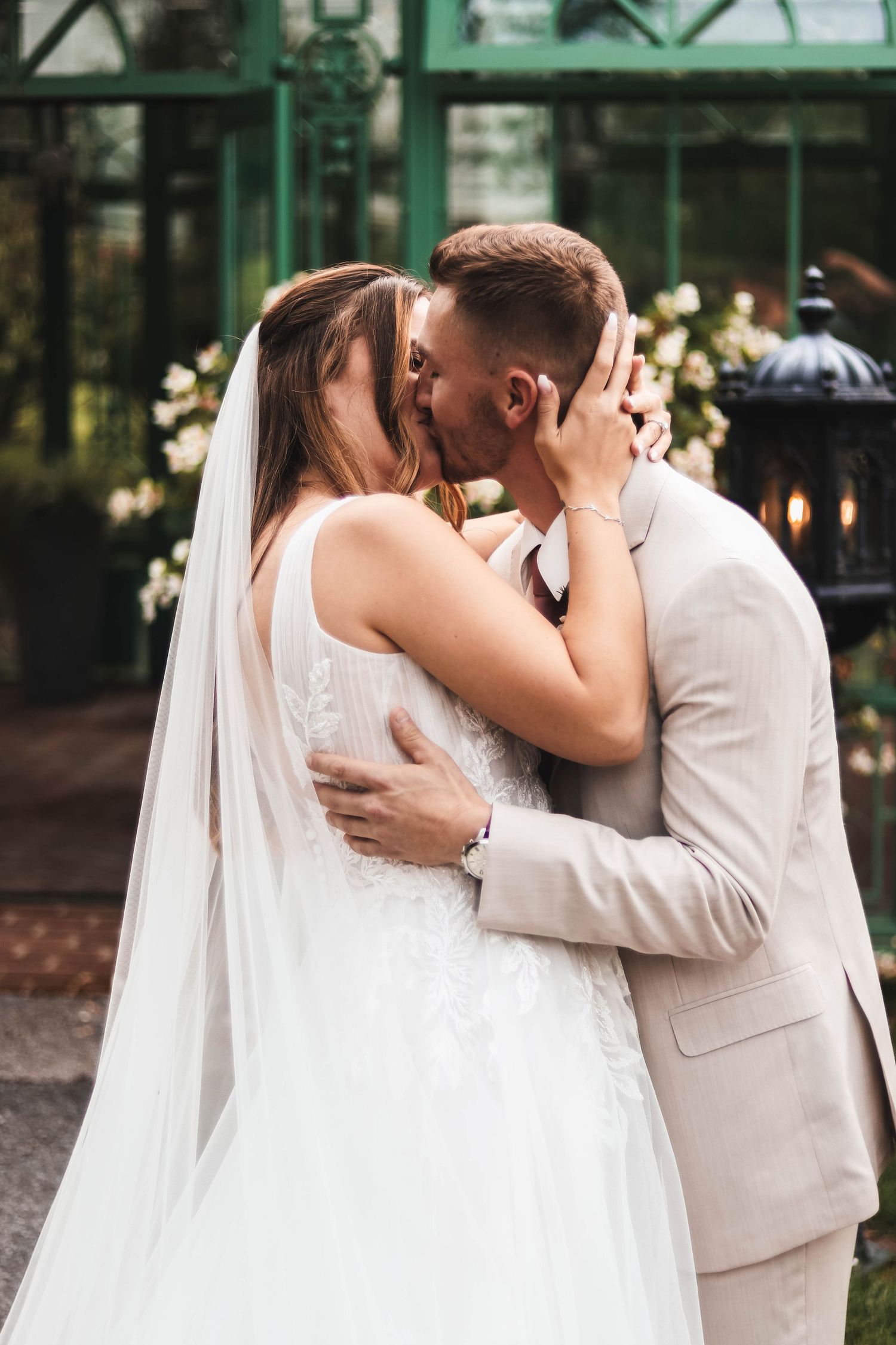 Bride and groom share a romantic first kiss in front of a green greenhouse on their wedding day in Lancaster..
