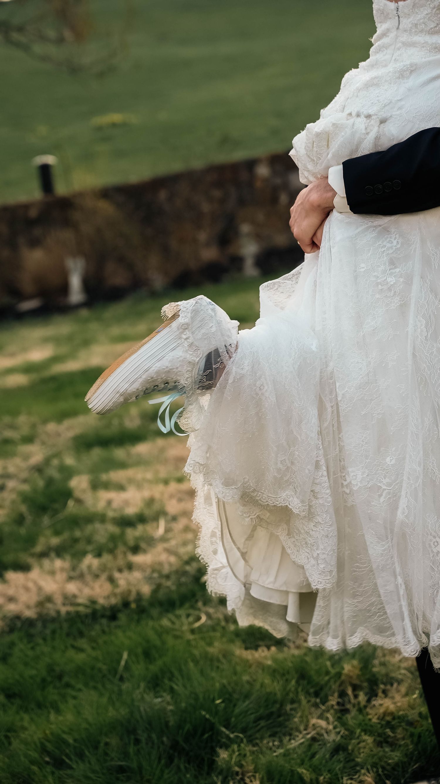 Groom scoops up bride in elegant lace wedding gown on green grass outdoors.