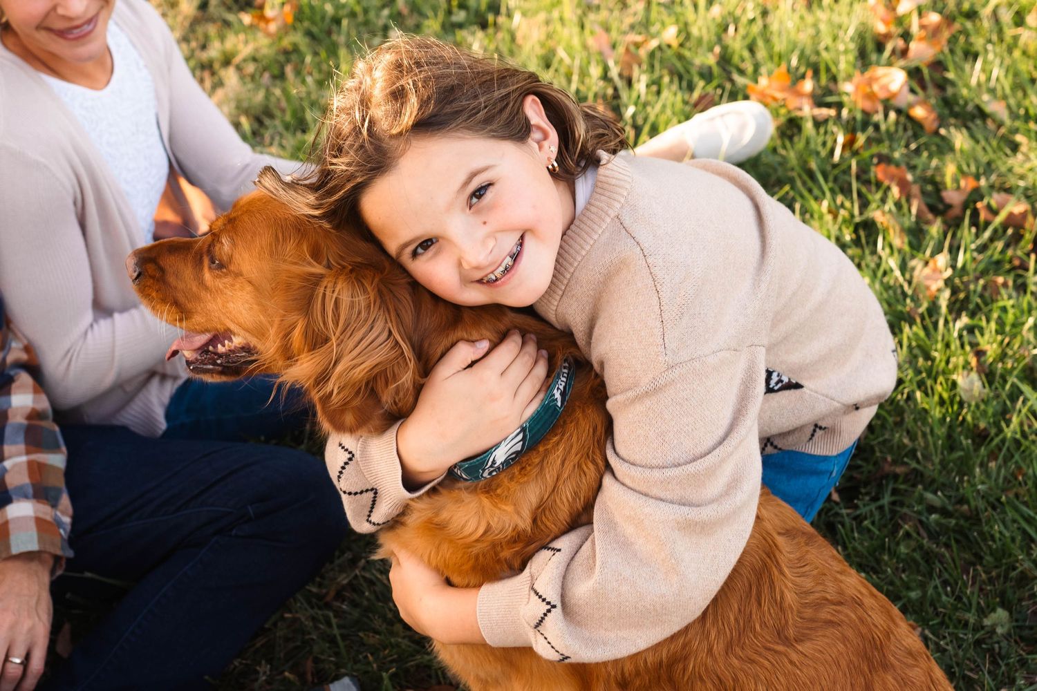 A smiling child hugs a golden retriever dog outdoors on green grass during autumn in Harleysville, PA.