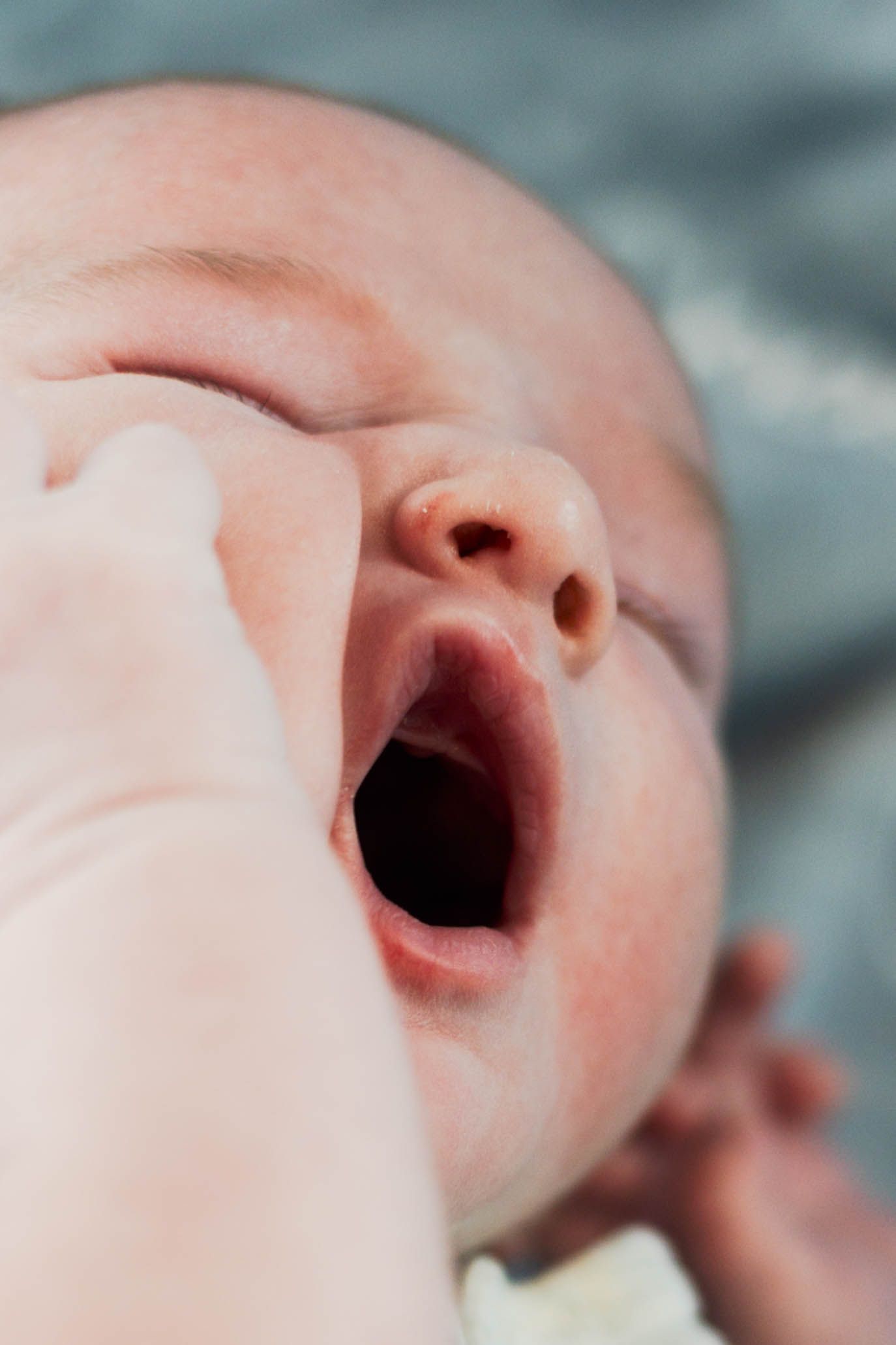 Adorable close-up of newborn baby yawning with tiny hand raised near face during an at home newborn session Philadelphia, PA.