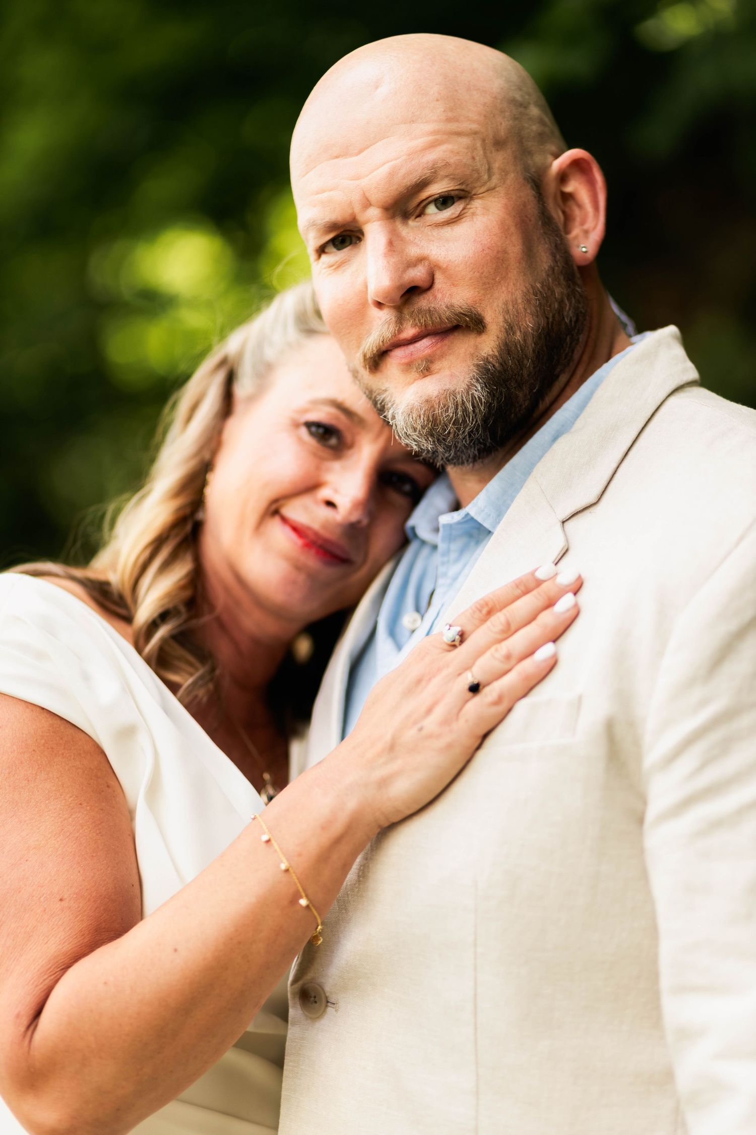 Couple embracing outdoors, bride in white resting her head on groom's chest in a linen suit In Perkiomenville, PA.