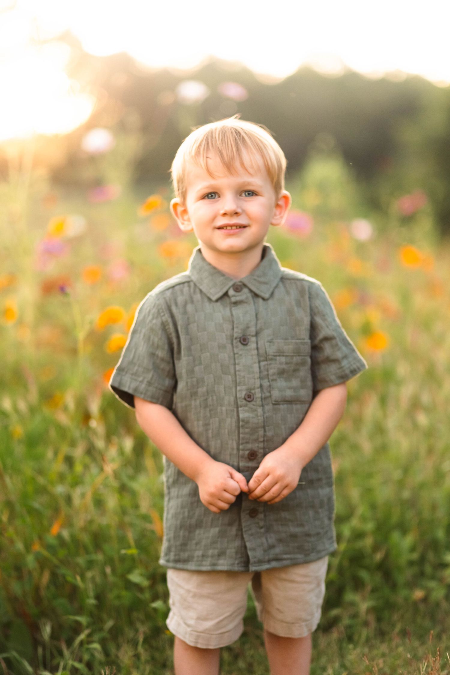 Smiling blonde boy in a green button-up shirt standing in a sunny wildflower field in Pekriomenville, PA.