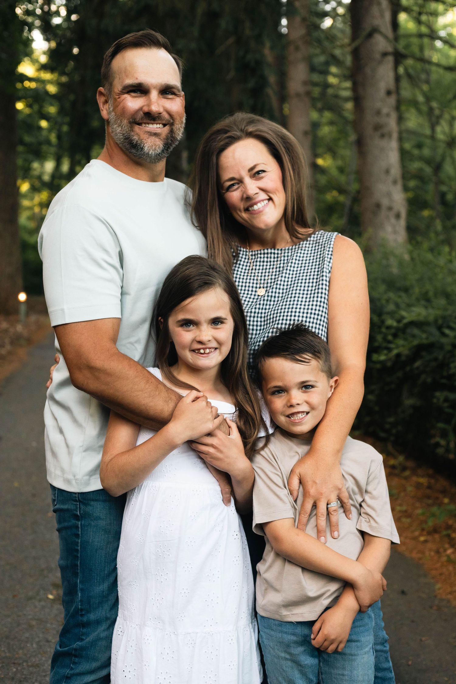 Happy family of four poses on a tree-lined path, parents embracing their young daughter and son outdoors in Boyertown, PA.