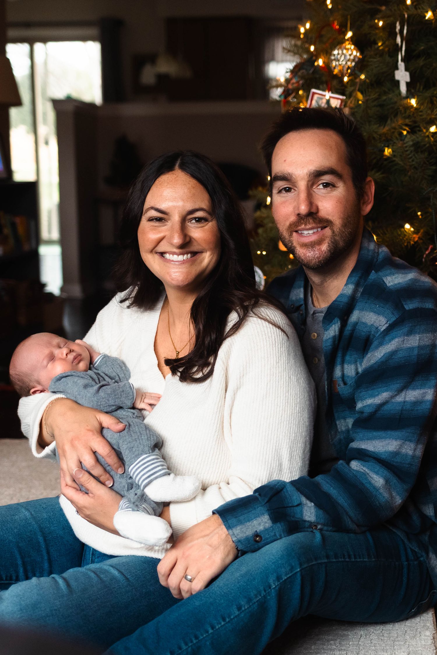 Smiling parents holding their newborn baby in front of a Christmas tree during an at home newborn session in Pottstown, PA.