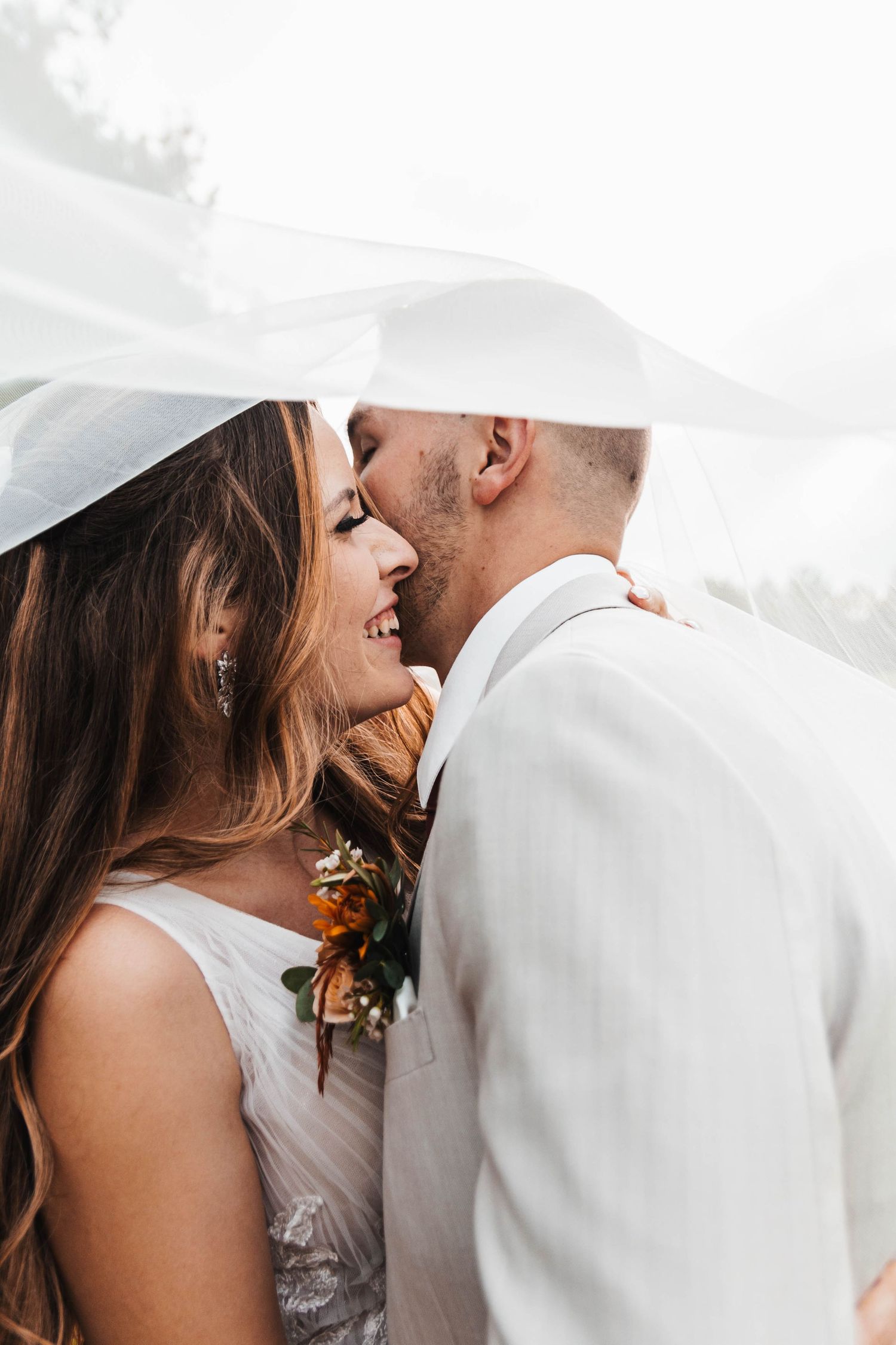 Bride and groom share a romantic kiss under a flowing white veil on their wedding day.