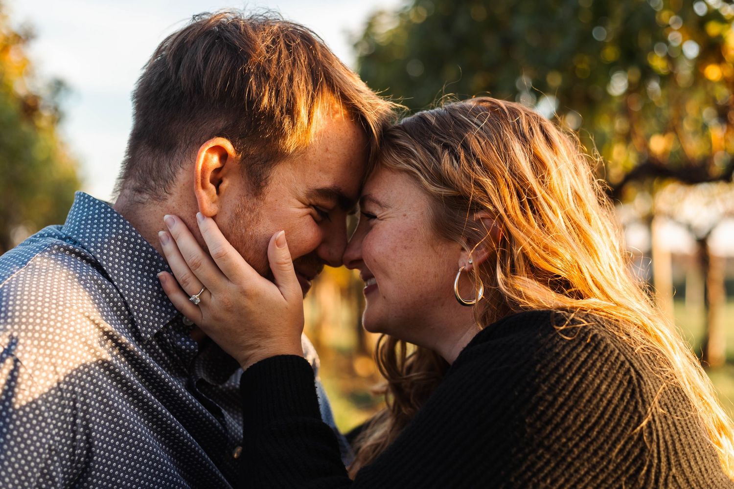 Couple sharing an intimate nose-to-nose moment outdoors with warm autumn bokeh background behind them in Lancaster, PA.