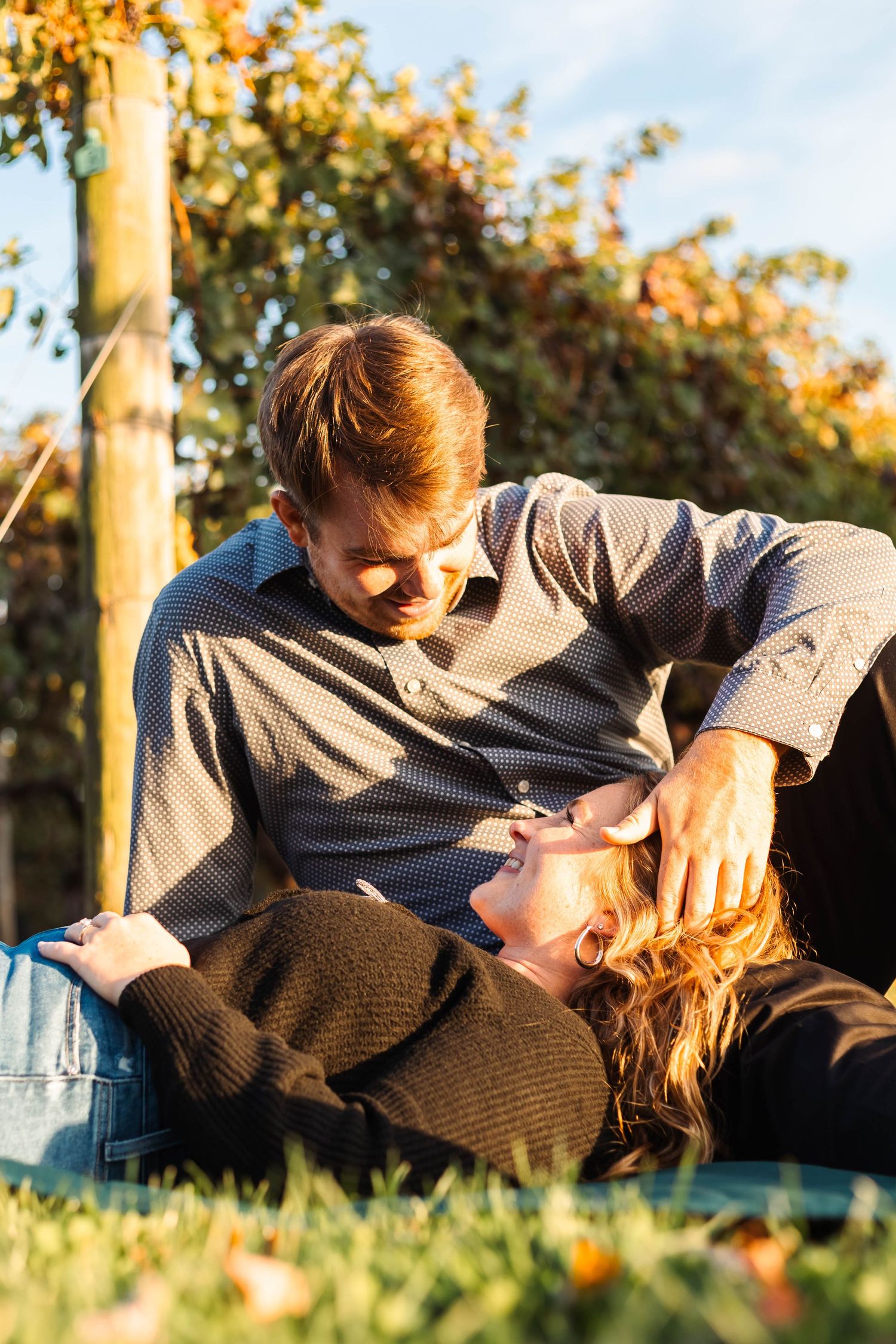 Couple relaxing on grass in sunny autumn garden, man gazing lovingly at woman lying in his lap in Lancaster, PA.