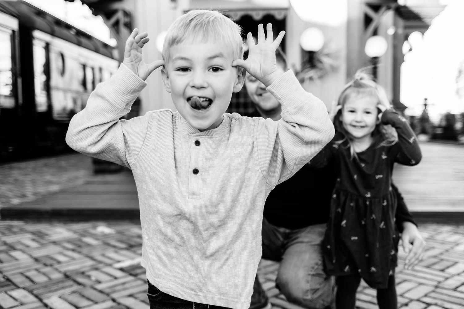 A boy makes a funny face with hands raised while his sister poses behind him in black and white at the Colebrookdale Railroad Station.