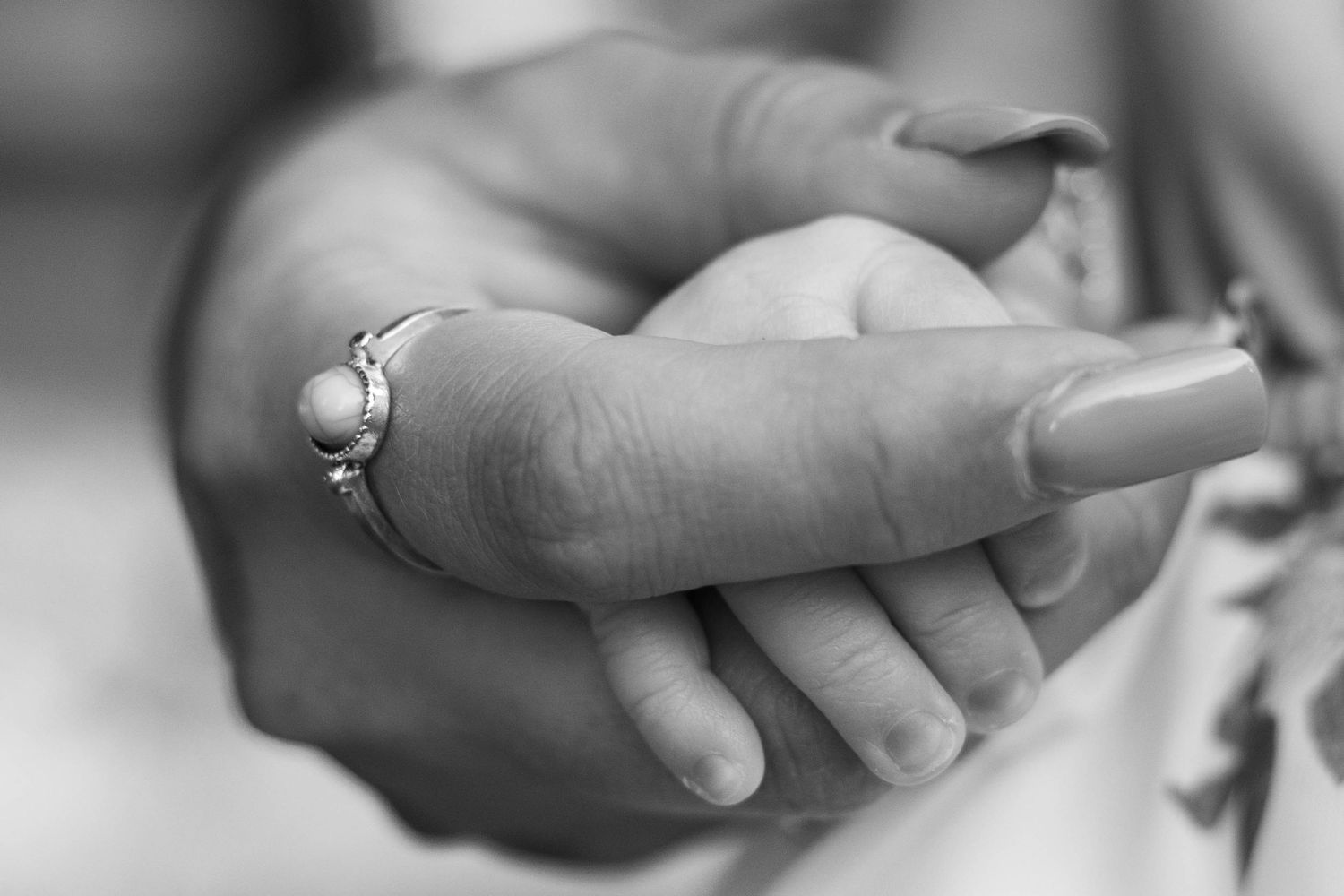 Black and white close-up of newborn baby's hand grasping mother's finger wearing a pearl ring during a newborn session in Boyertown, PA.