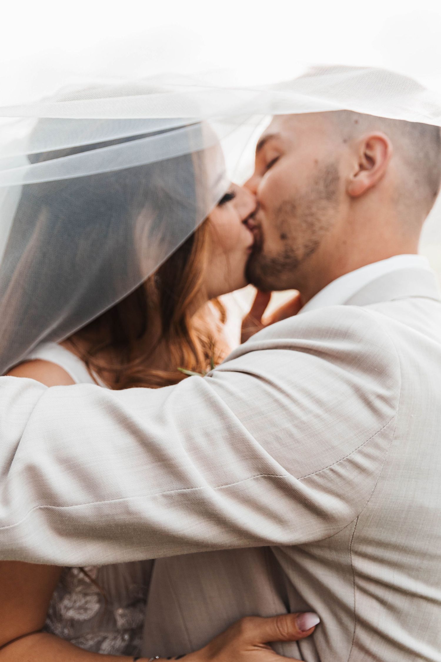 Bride and groom share a passionate kiss under a flowing white veil in a romantic close-up portrait in Lancaster..