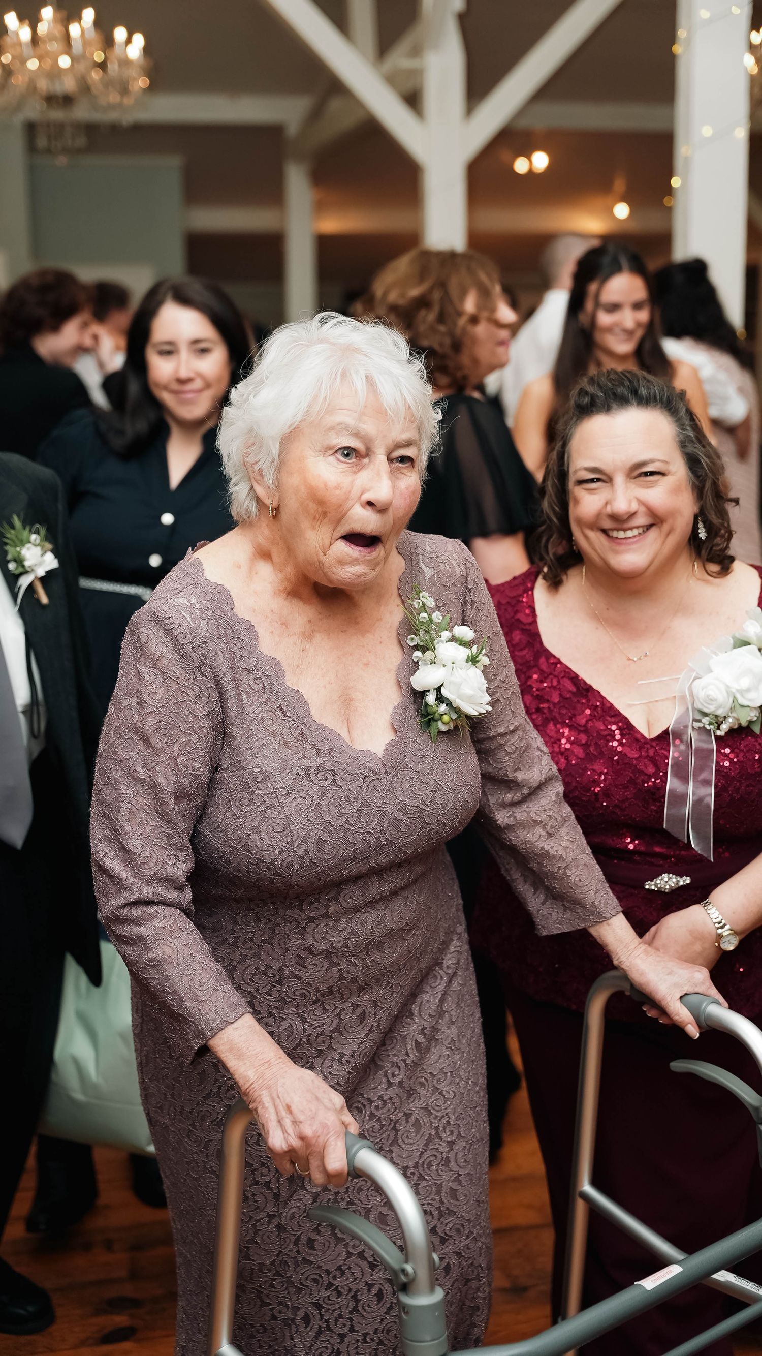 Elderly grandmother with walker and smiling woman in burgundy dress at festive wedding reception celebration.
