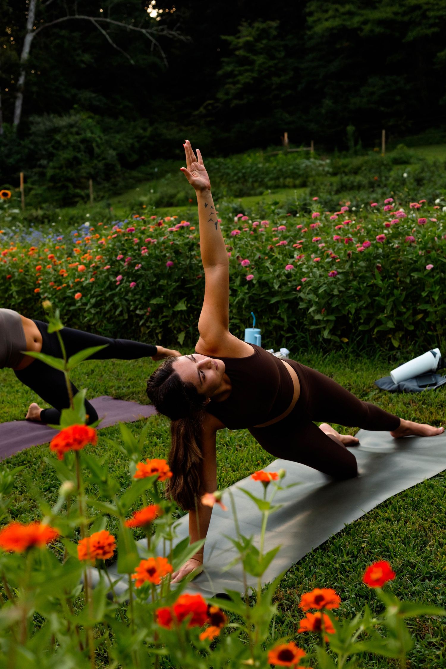 Woman performs a side angle yoga pose on a mat in a vibrant outdoor flower garden at sunset.