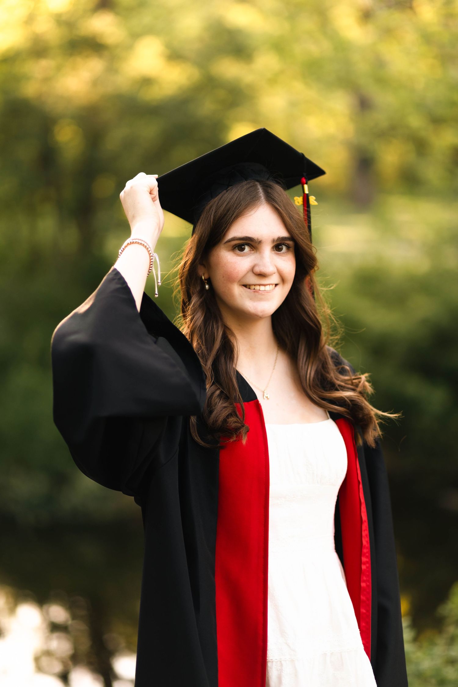 Smiling Boyertown Senior in black graduation gown and cap holding tassel outdoors with green trees in background.