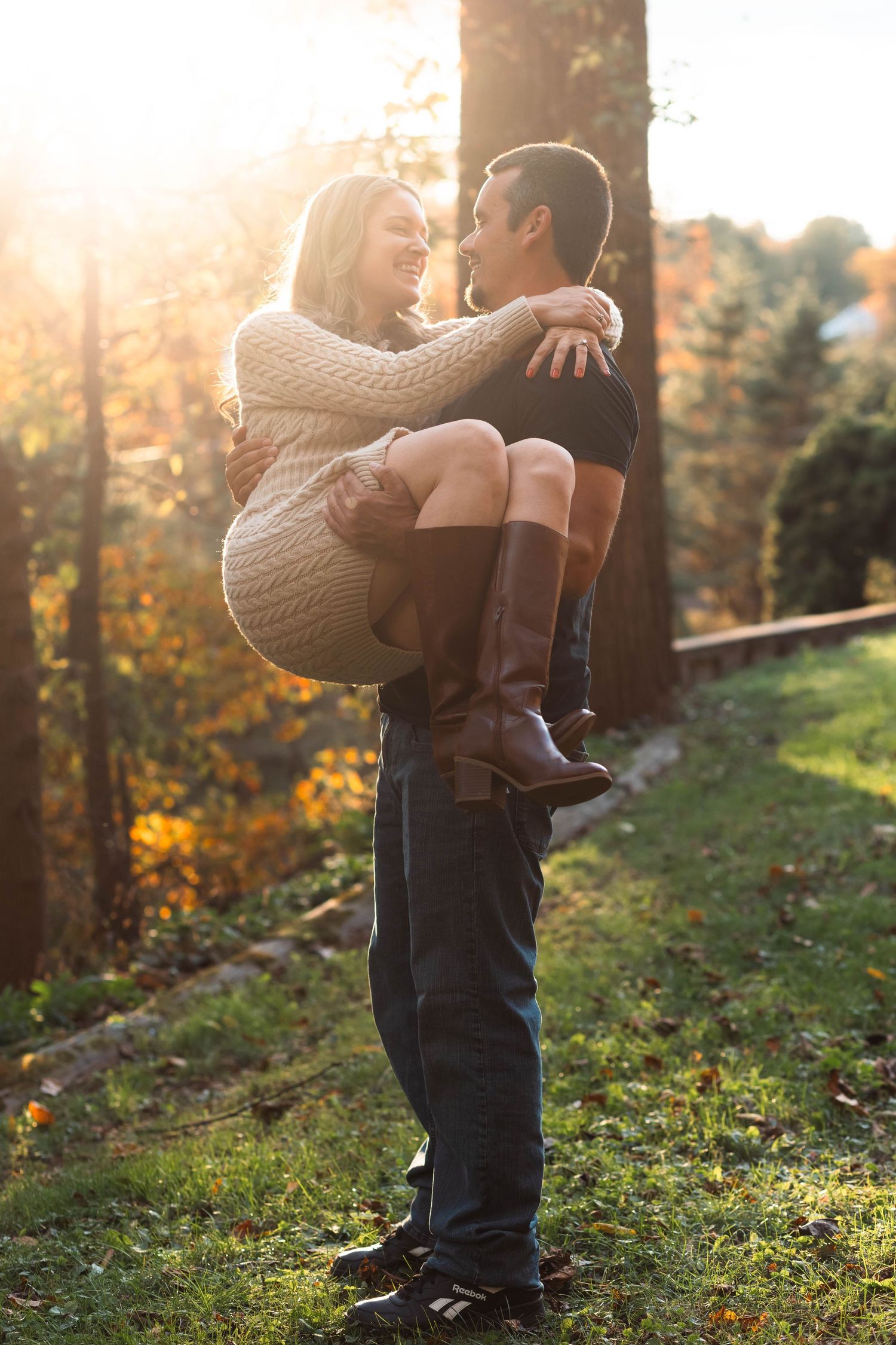 Man lifting woman in his arms in a sunny autumn park, both smiling joyfully at each other in Boyertown, PA.