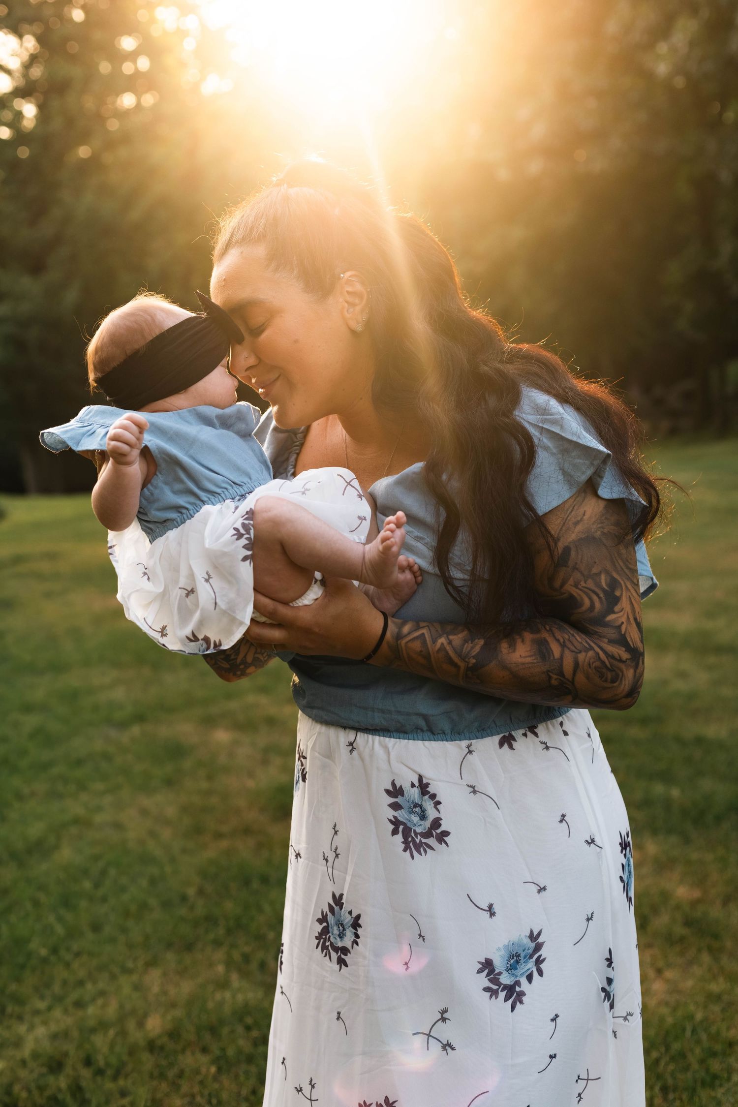Mother holding newborn baby in golden sunset light in a lush green park.