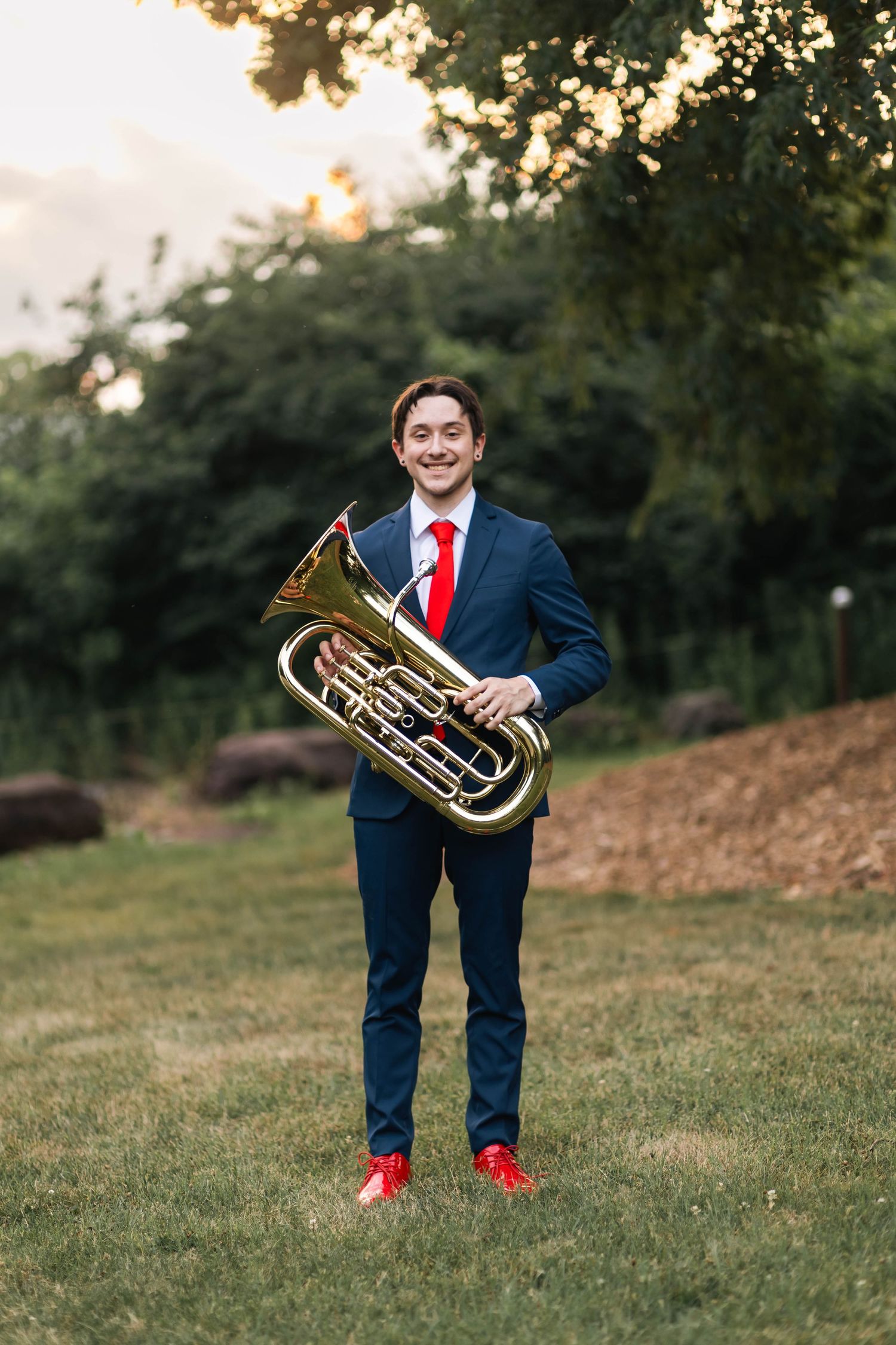 Owen J Roberts High School Senior in navy suit holds euphonium brass instrument on green lawn.