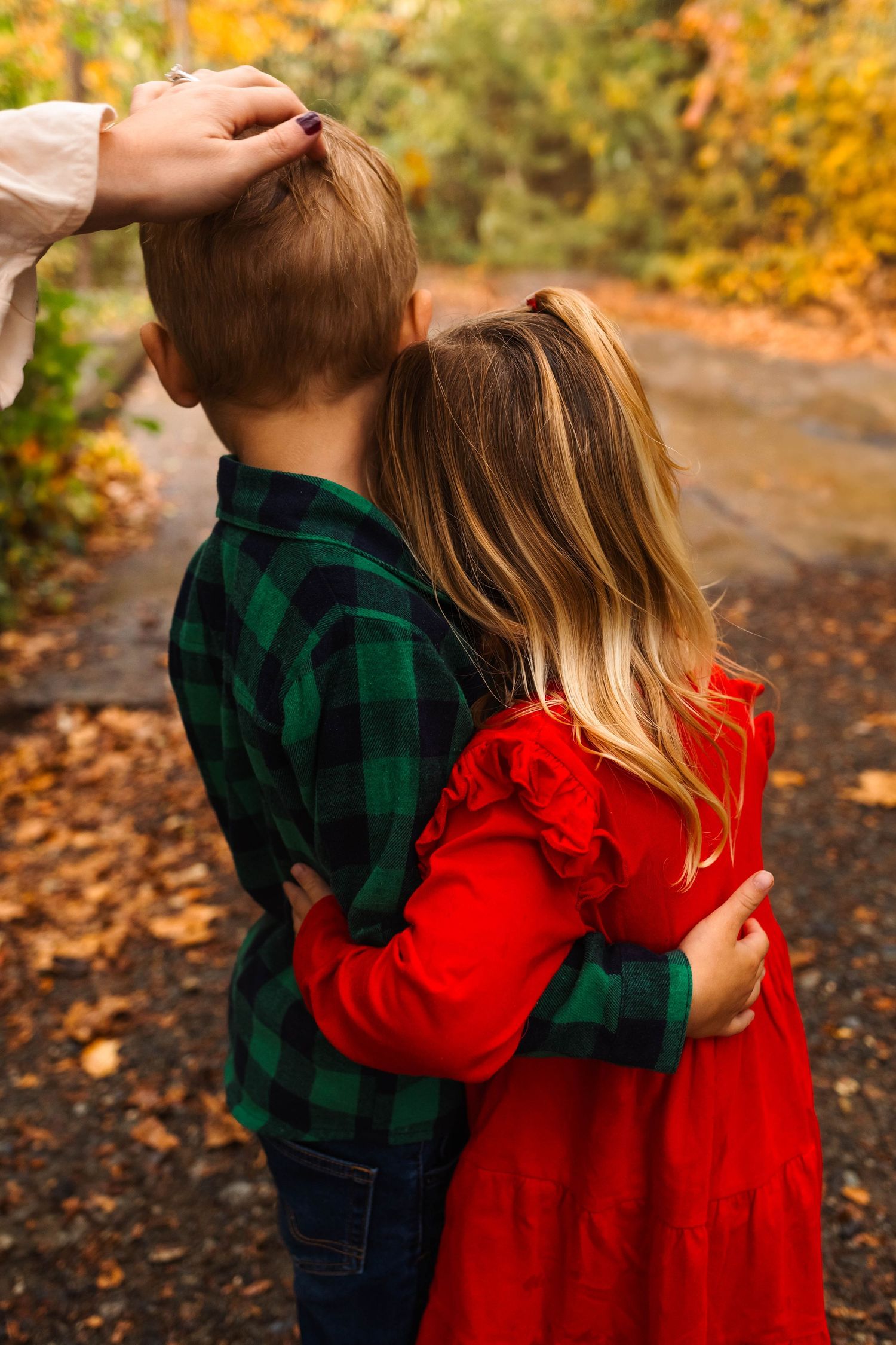 Two young siblings share a sweet hug on a leaf-covered path surrounded by vibrant autumn foliage in Pottstown, PA.