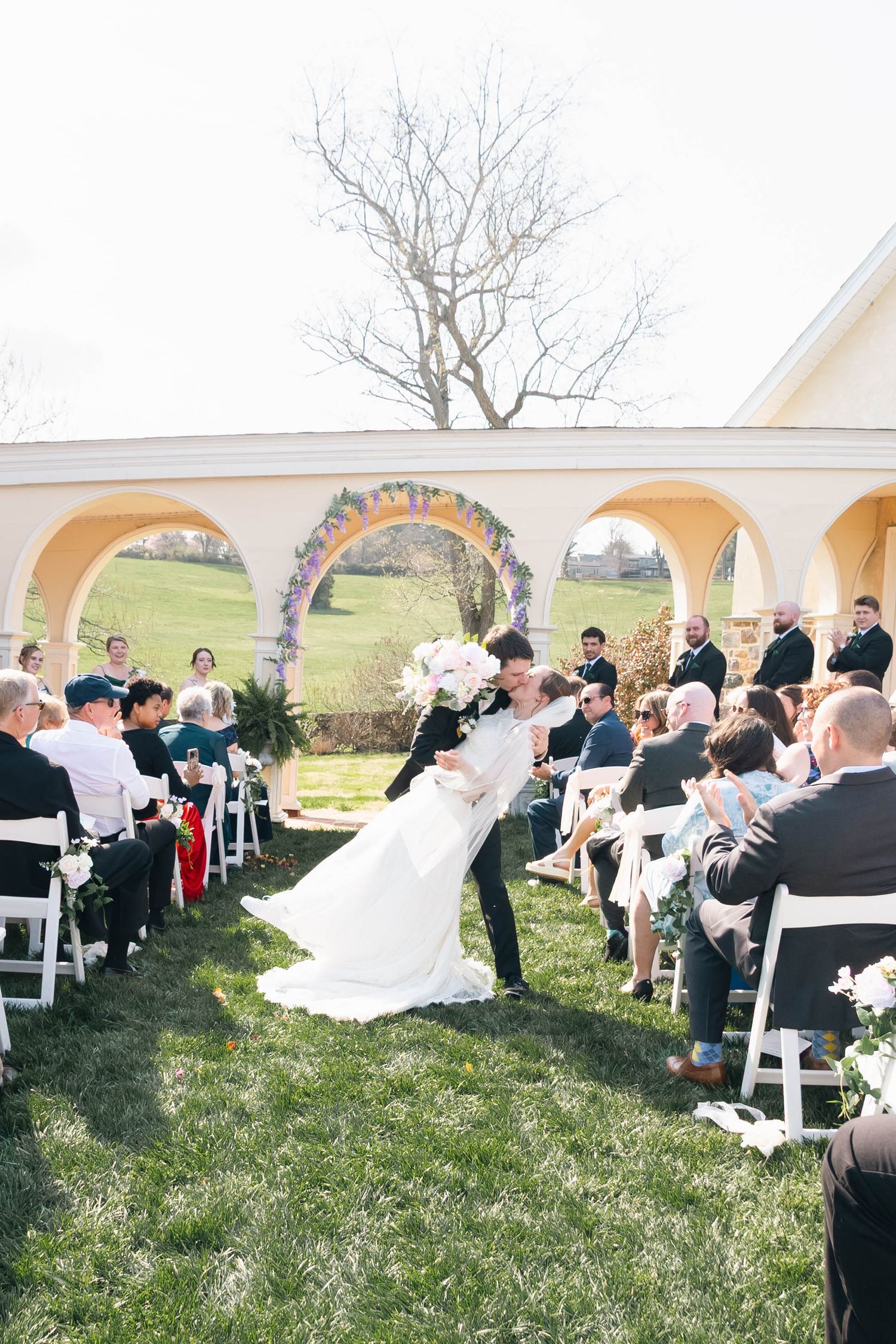 Groom dips bride for a kiss while walking down the aisle at outdoor wedding ceremony.