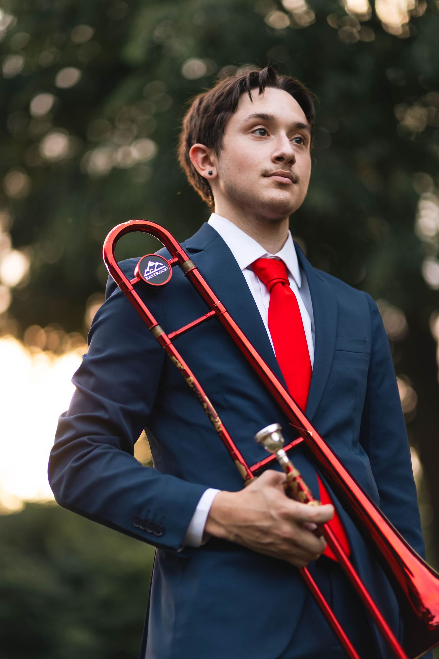 Owen J Roberts High School Senior in navy suit holds red trombone while looking up in outdoor setting.