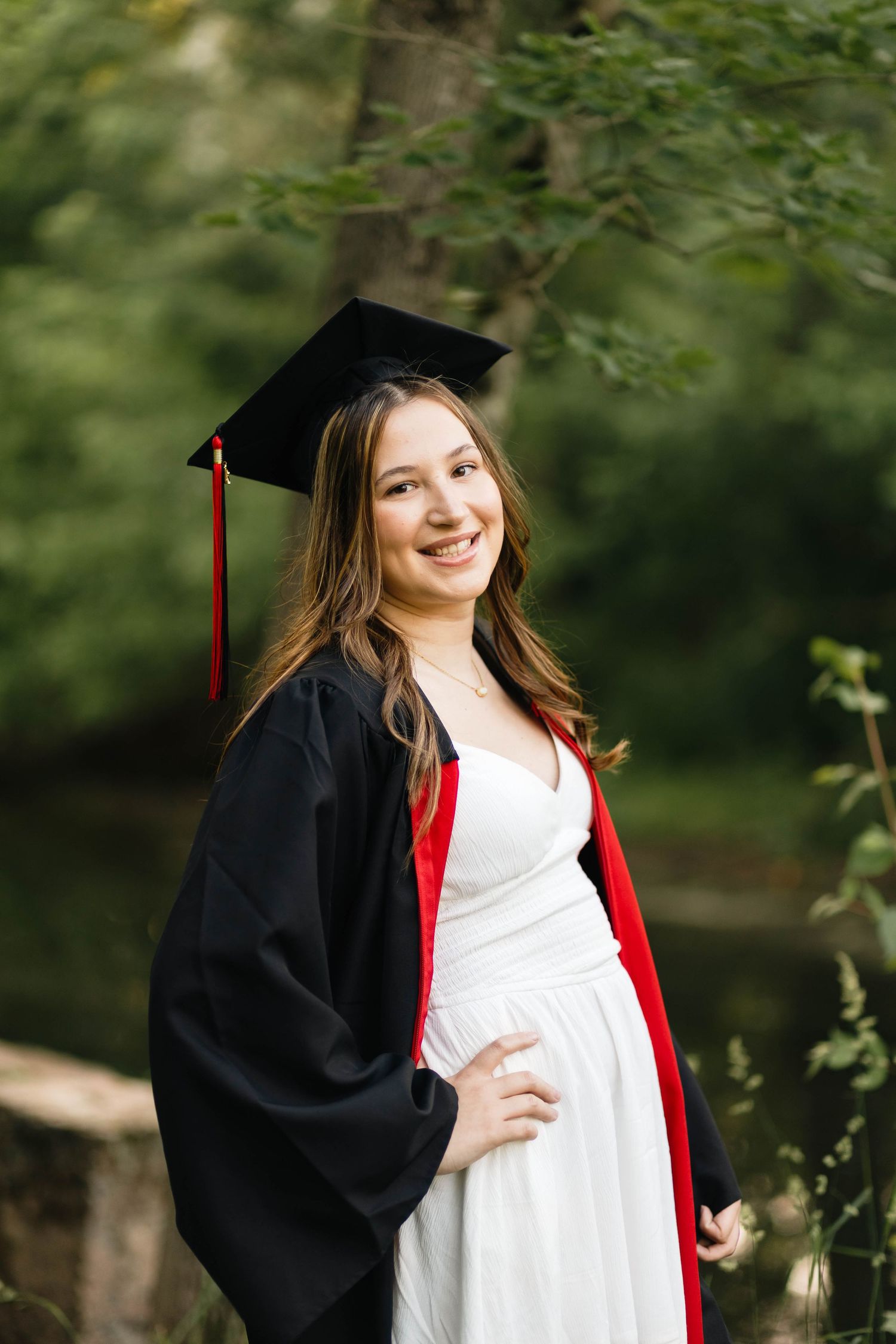 Boyertown Senior in graduation cap and gown with red stole smiling outdoors among green trees.