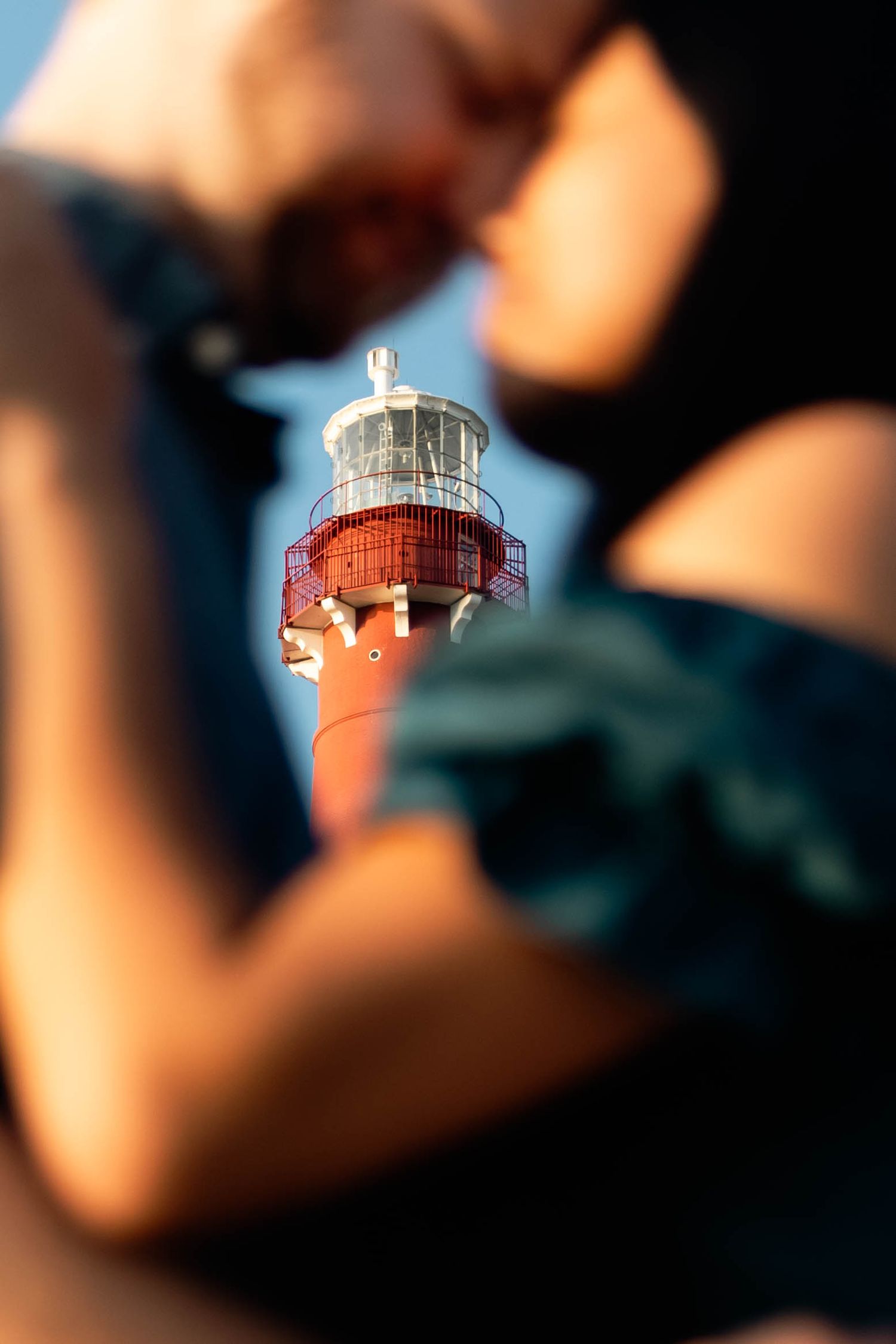 Creative blurred foreground shot framing a red and white lighthouse top against a blue sky in Barnegat, NJ.