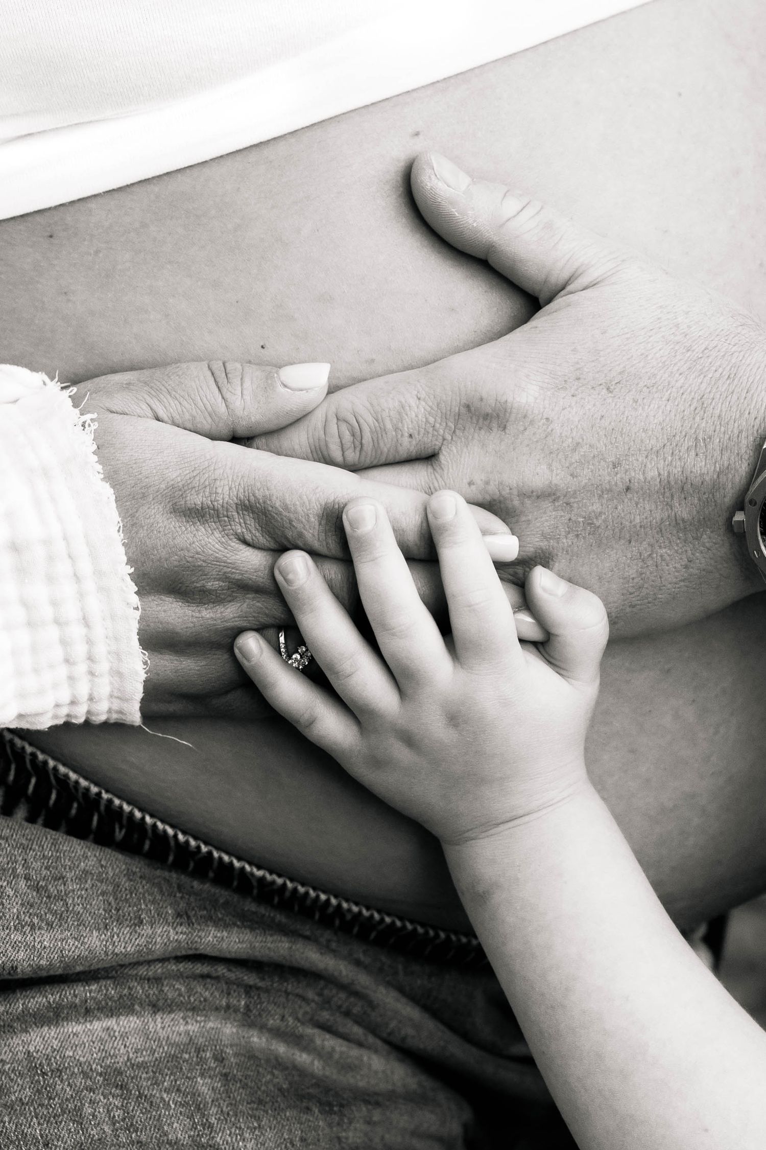 Black and white photo of a childs small hand touching a pregnant womans belly alongside adult hand at Hopewell Furnace in Elverson, PA.
