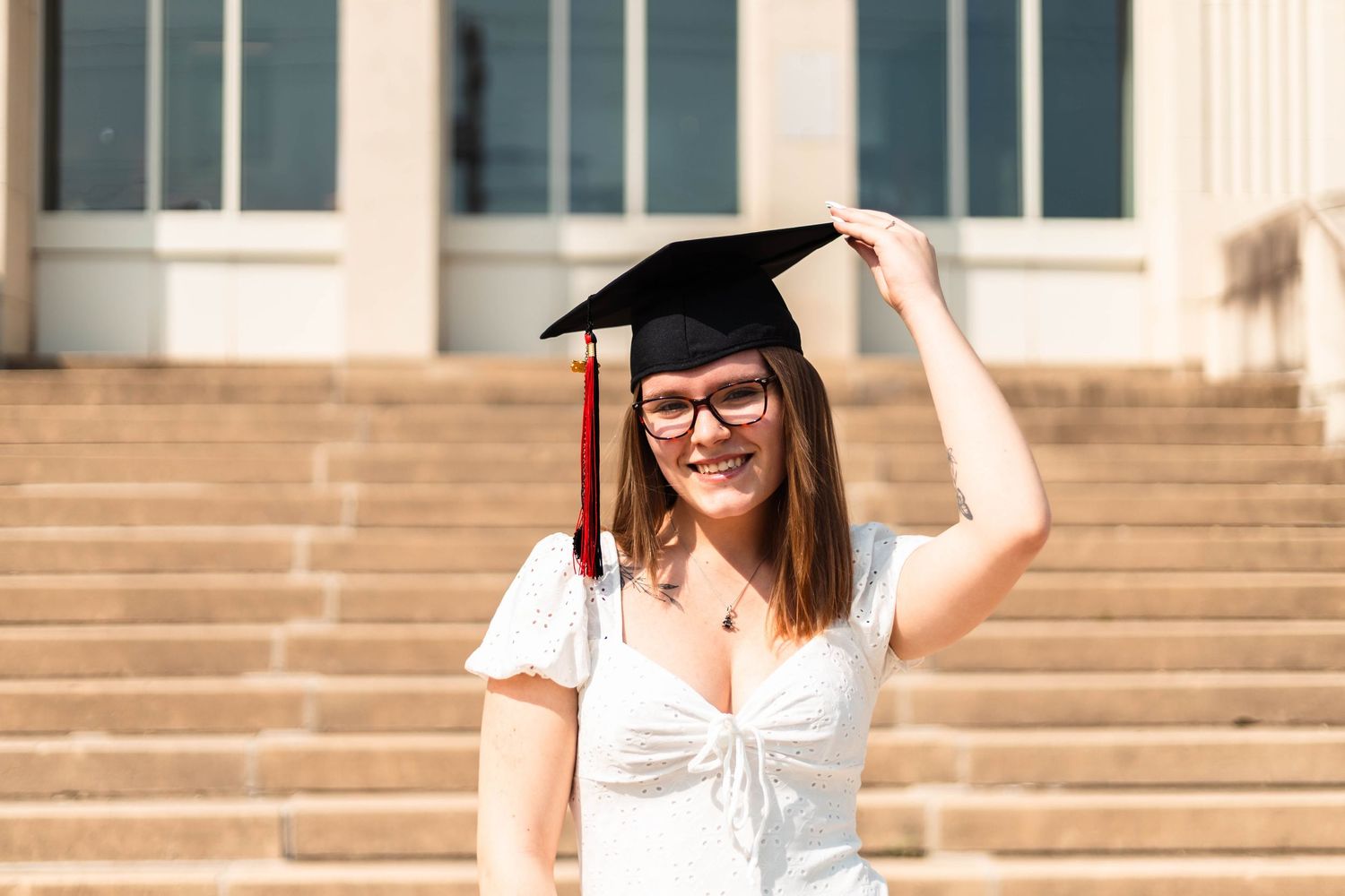 Smiling Boyertown graduate in white dress and cap standing on university steps in bright sunlight.