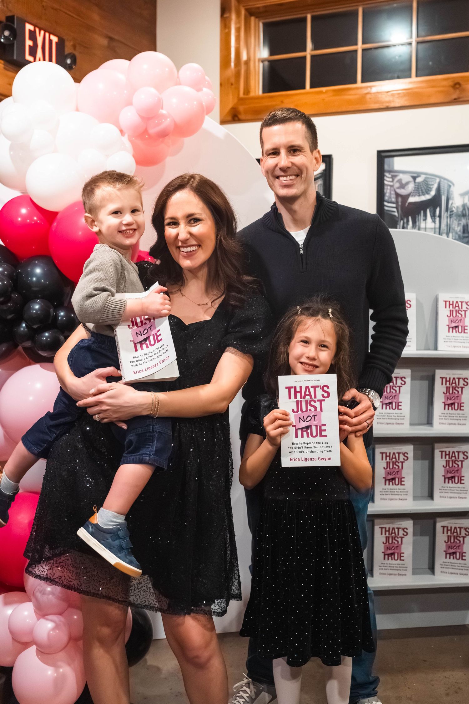A family of four poses with copies of the book That's Just Not True at a book launch event with balloons at Brakeman Cafe in Boyertown, PA.
