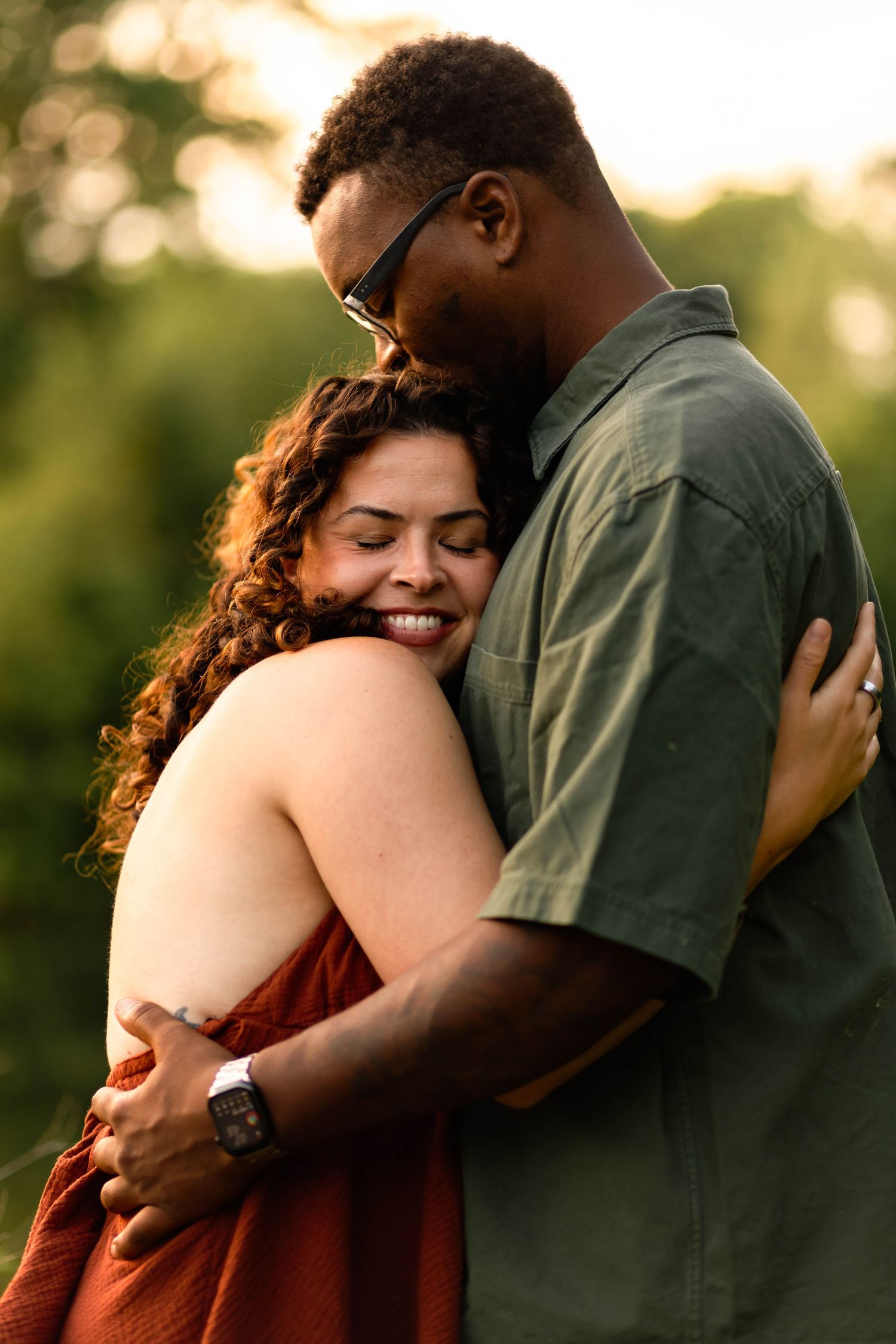 A smiling woman in a red top embraces a tall man in a green shirt during a golden sunset outdoors at Grings Mill in Reading, PA.