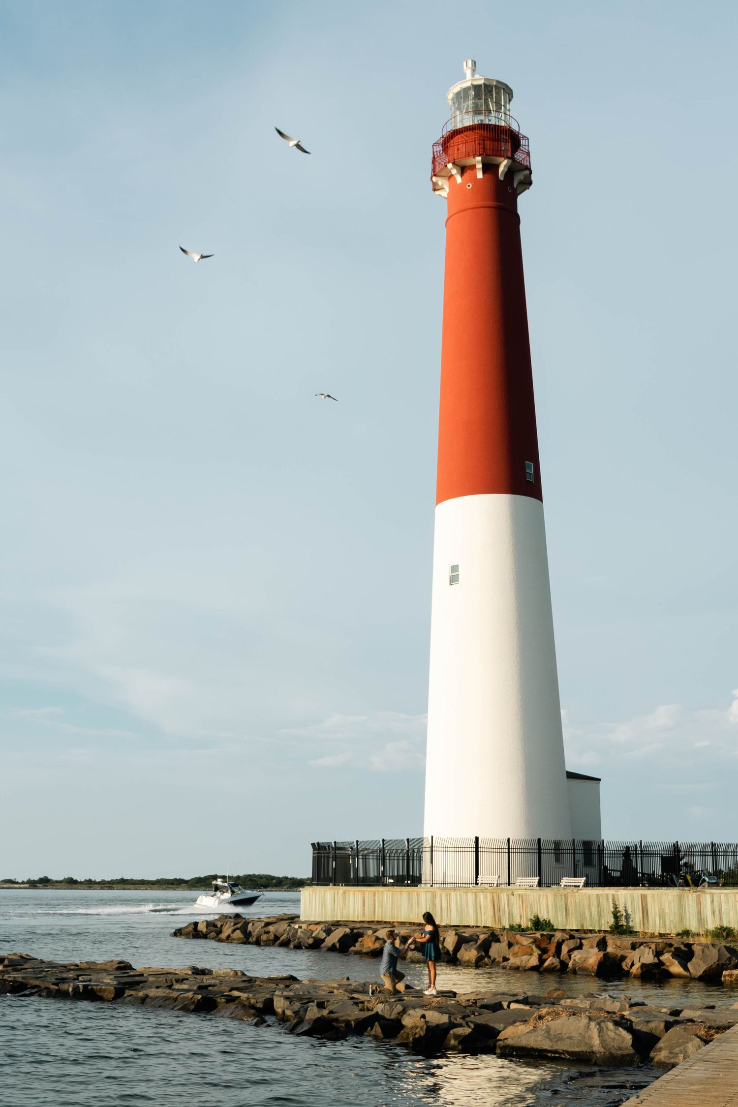 Tall red and white striped lighthouse stands against a blue sky with seagulls flying overhead in Barnegat, NJ.