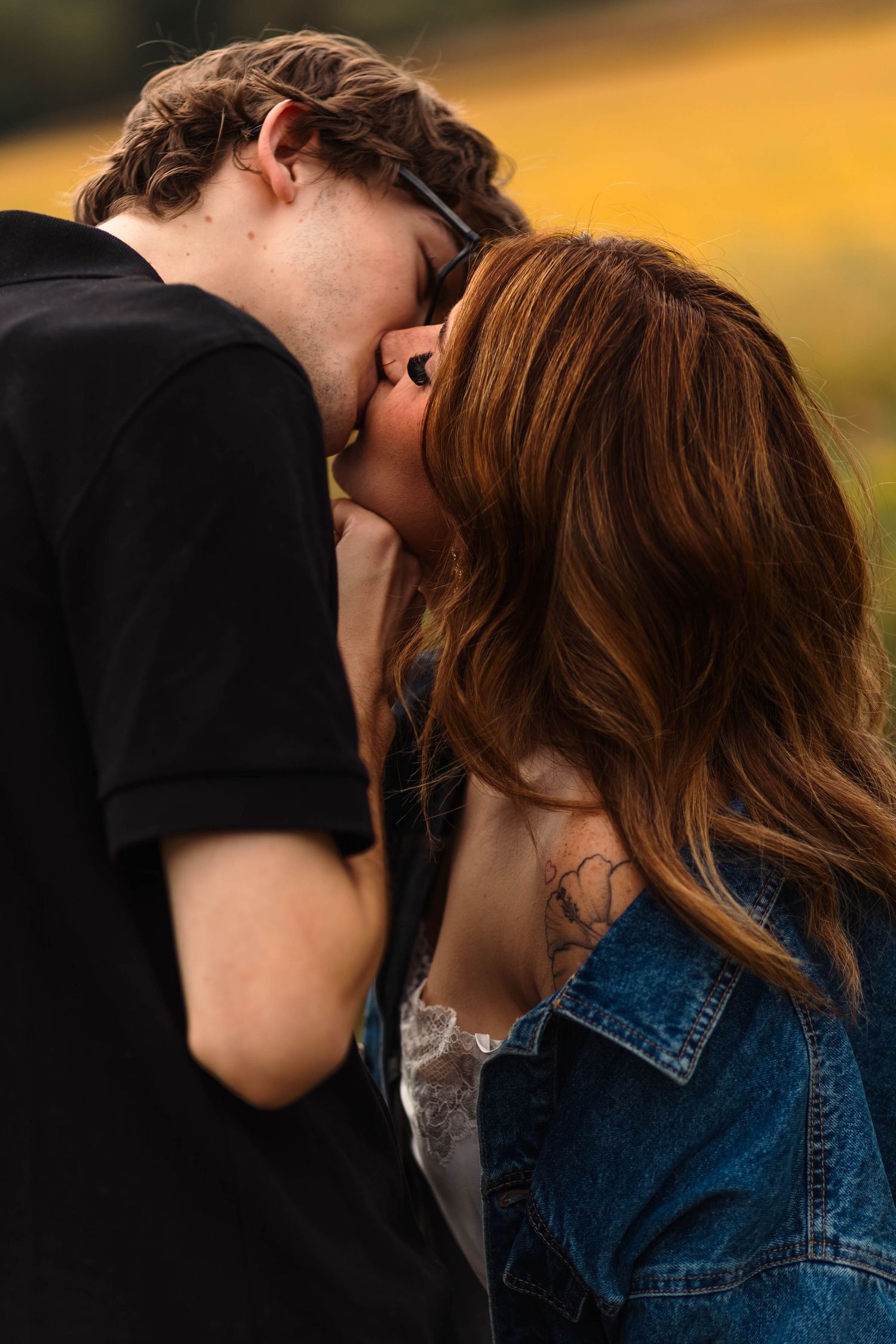 Young couple sharing a kiss outdoors in golden field at sunset.