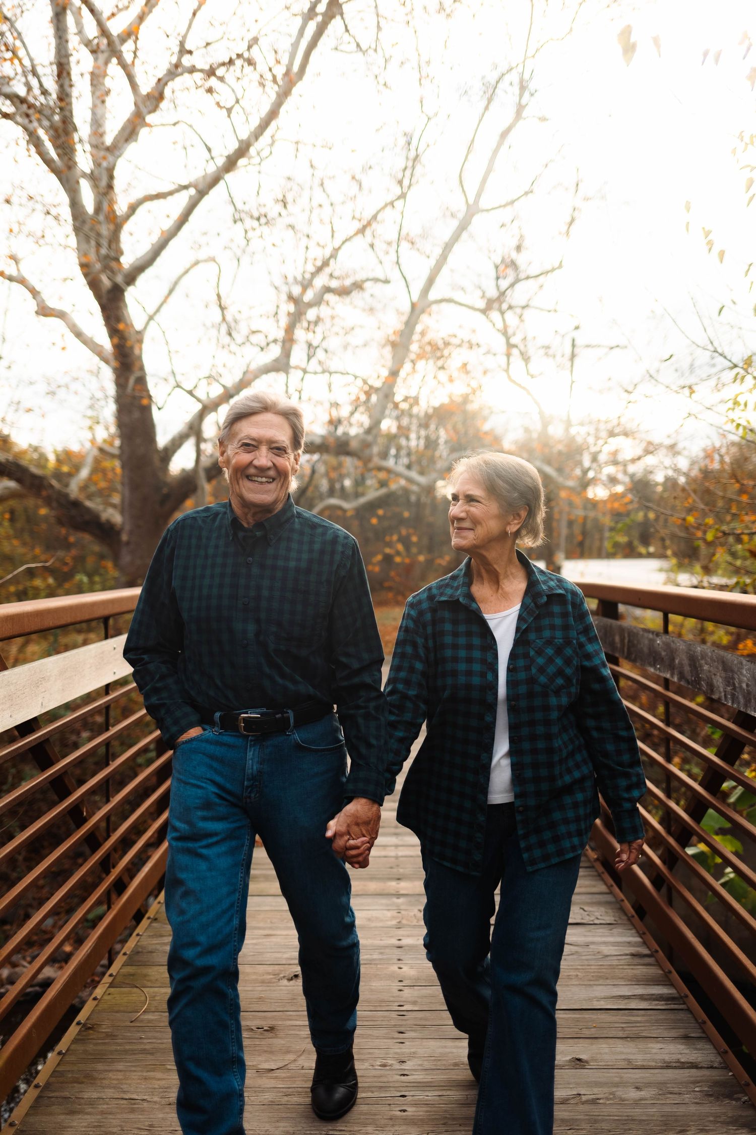 Senior couple holding hands walking on wooden bridge in autumn park setting.