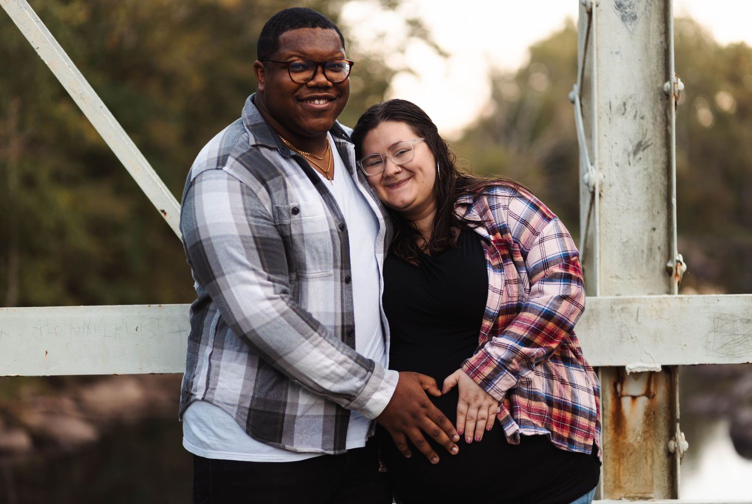 Smiling interracial couple posing together on a white bridge railing with soft natural background at Green Lane, Park.