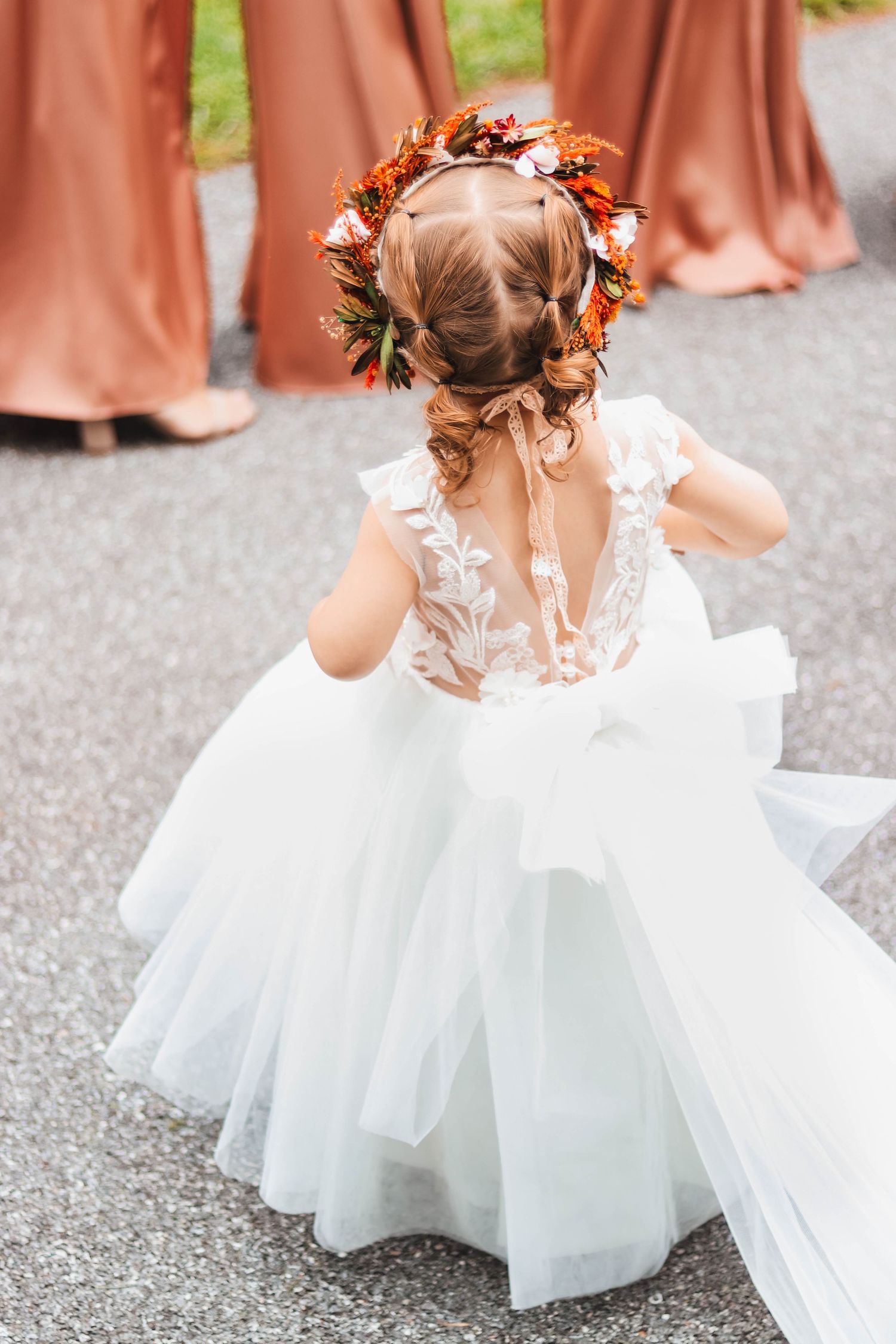 Flower girl in white tulle dress with autumn floral crown walks toward bridesmaids in dusty rose gowns.