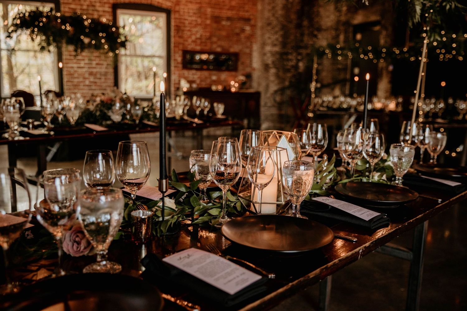Sophisticated wedding reception table set with black plates, crystal glasses, and greenery.